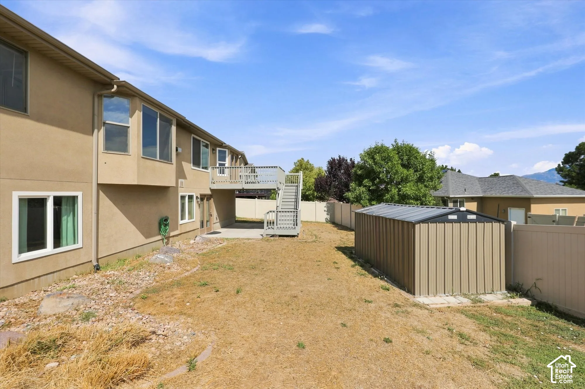 Exterior backyard space featuring a concrete patio, raised wooden deck with stairs, a metallic storage shed, and perimeter vinyl fencing