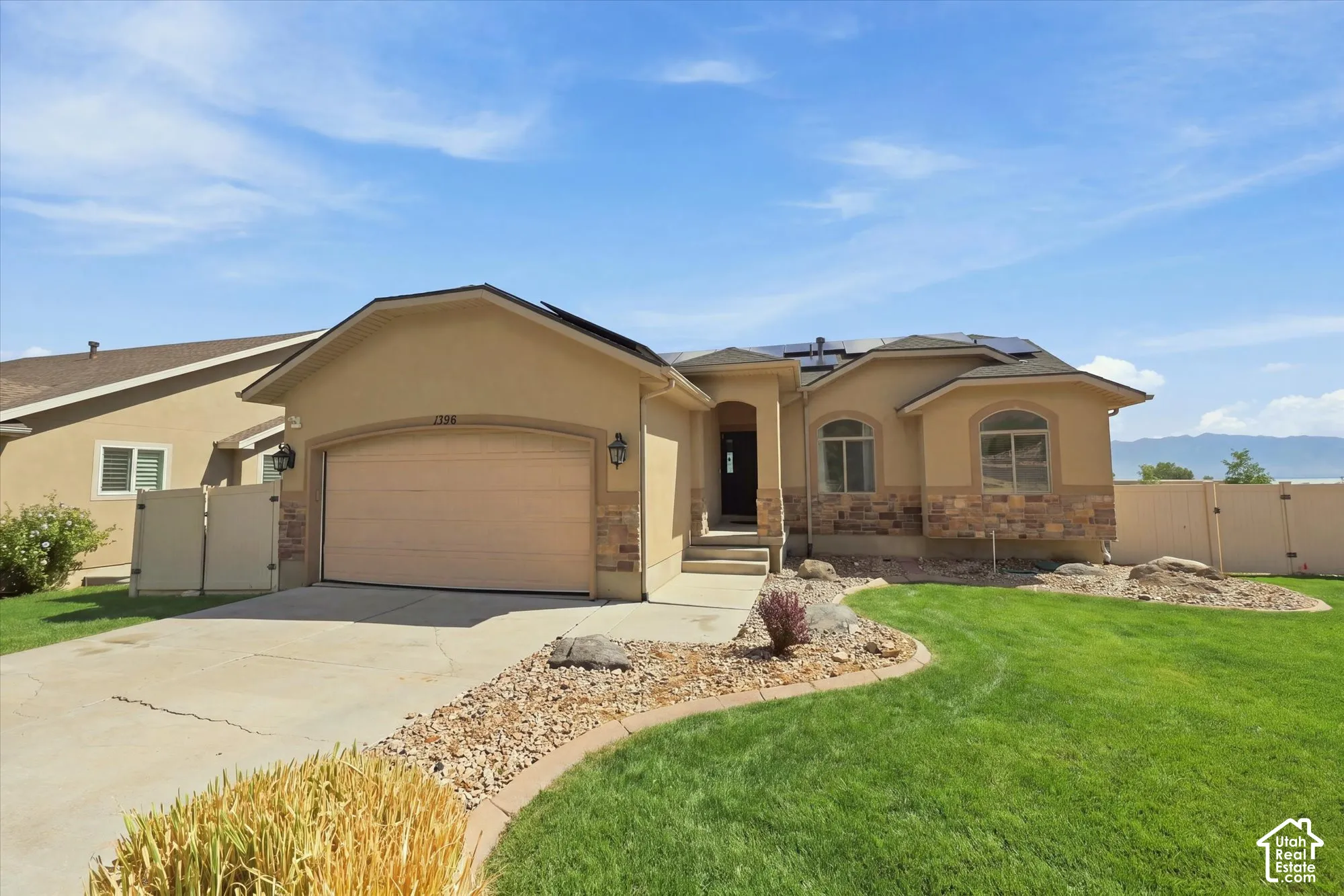 Stucco exterior with stone veneer accents, arched windows, attached garage, rooftop solar panels, and landscaped front yard