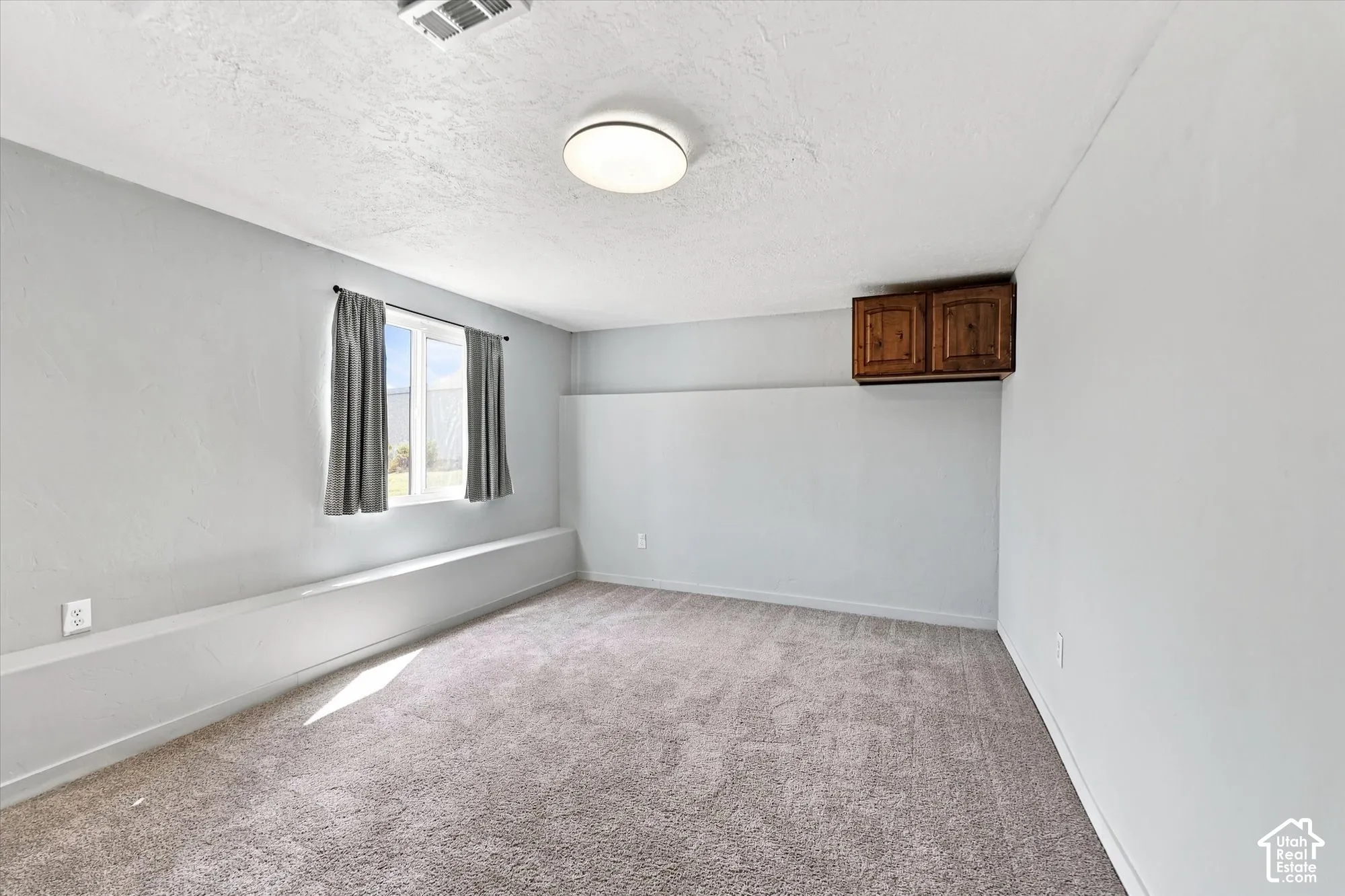 Neutral-toned carpeting, flush-mount ceiling lighting, window with a sill ledge, and wall-mounted wooden cabinetry