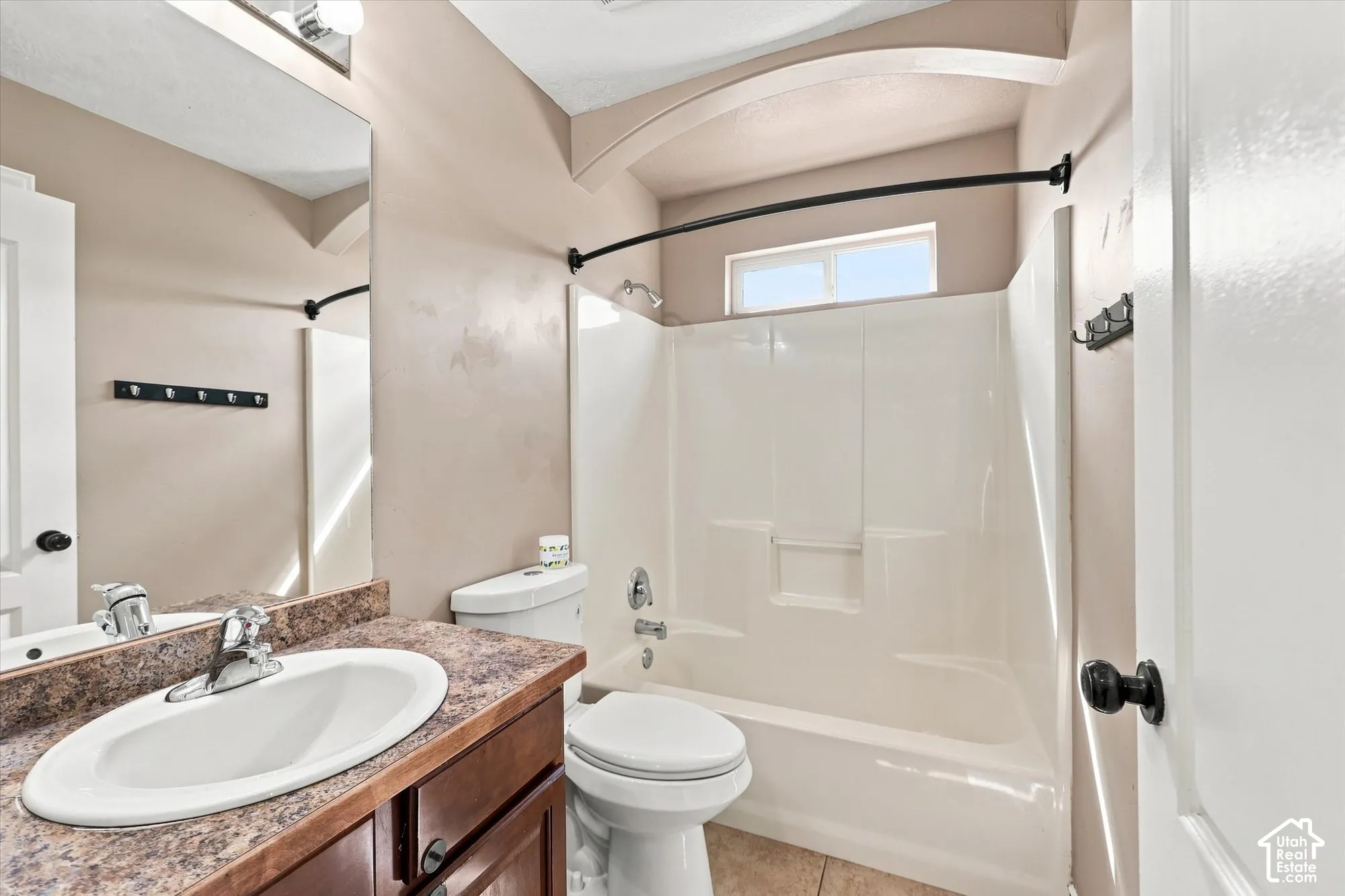 Bathroom featuring a stone-finish countertop, oval drop-in sink, arched ceiling detail, and a shower-tub combination with a built-in surround