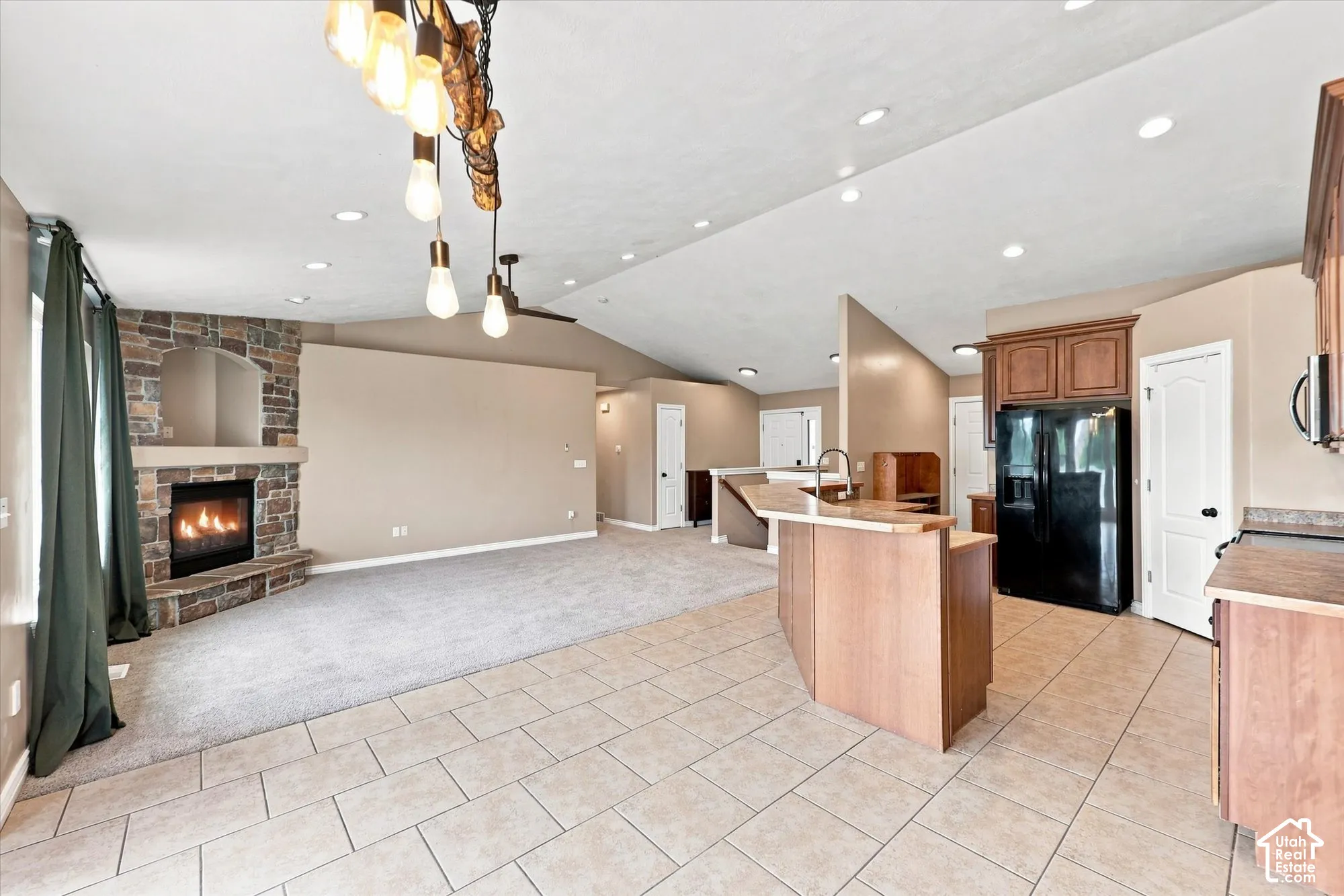 Vaulted ceiling featuring recessed lighting, floor-to-ceiling stone-faced fireplace with a built-in mantle, tile flooring, and a multi-tiered kitchen peninsula