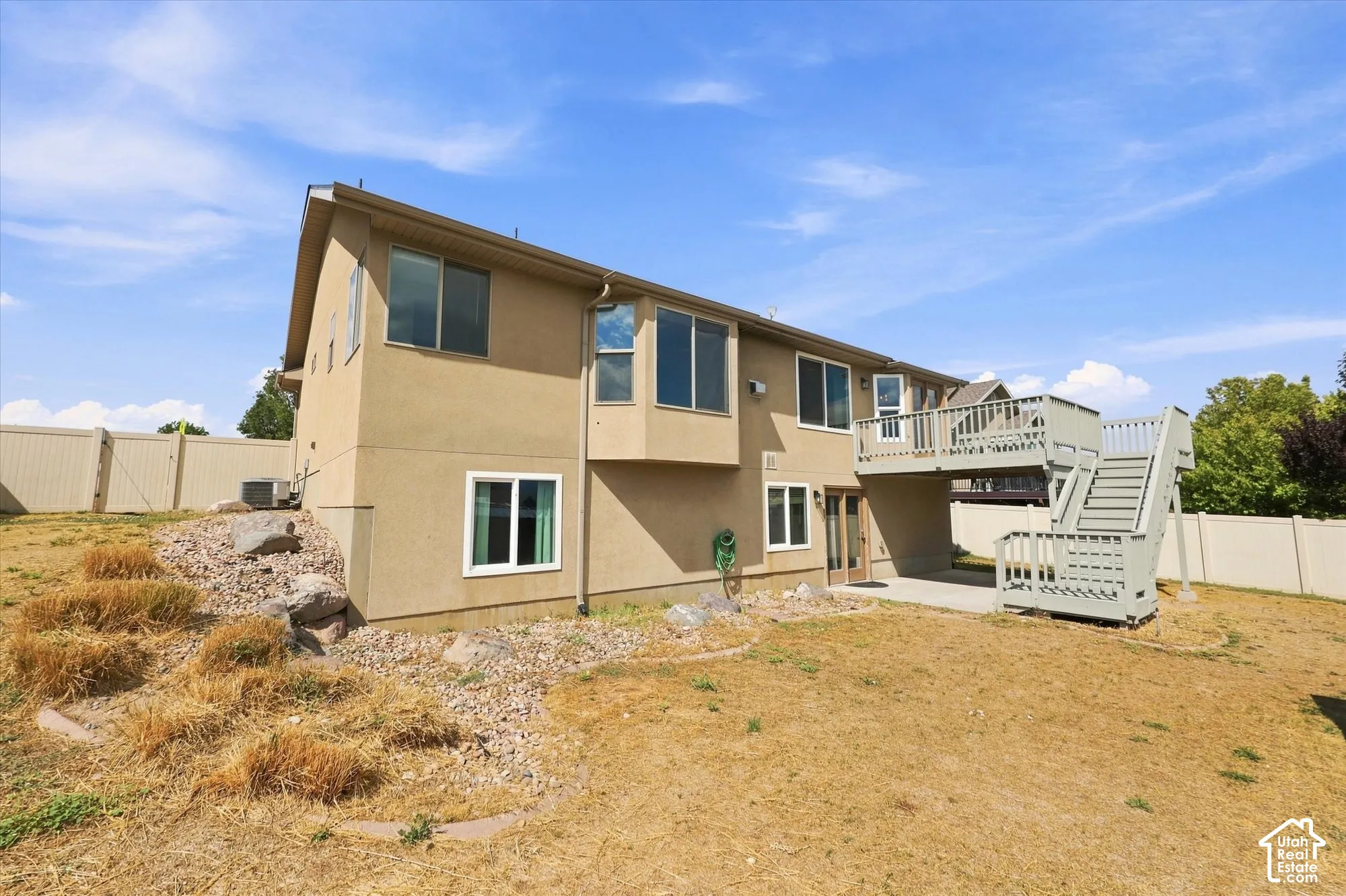 Stucco exterior featuring an elevated wood deck with stairs, double-pane windows, and a partially covered patio area