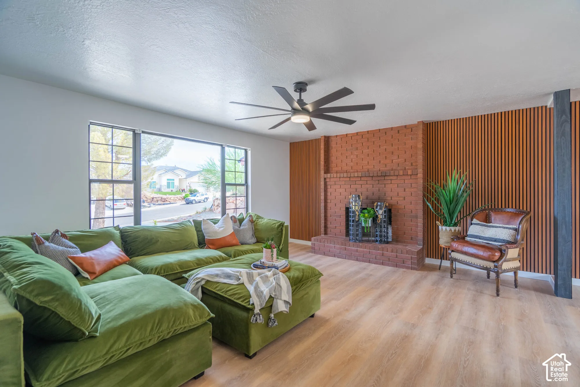 Spacious living area featuring a brick fireplace, wood-finish flooring, a contemporary ceiling fan, and a wood slat accent wall