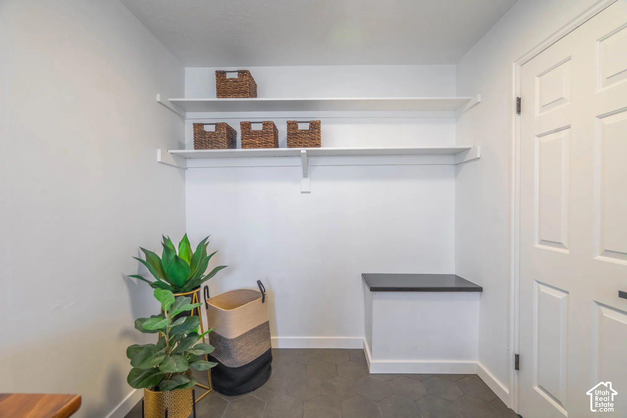 White walls, two white floating shelves, dark tile flooring, and a built-in counter with a dark surface