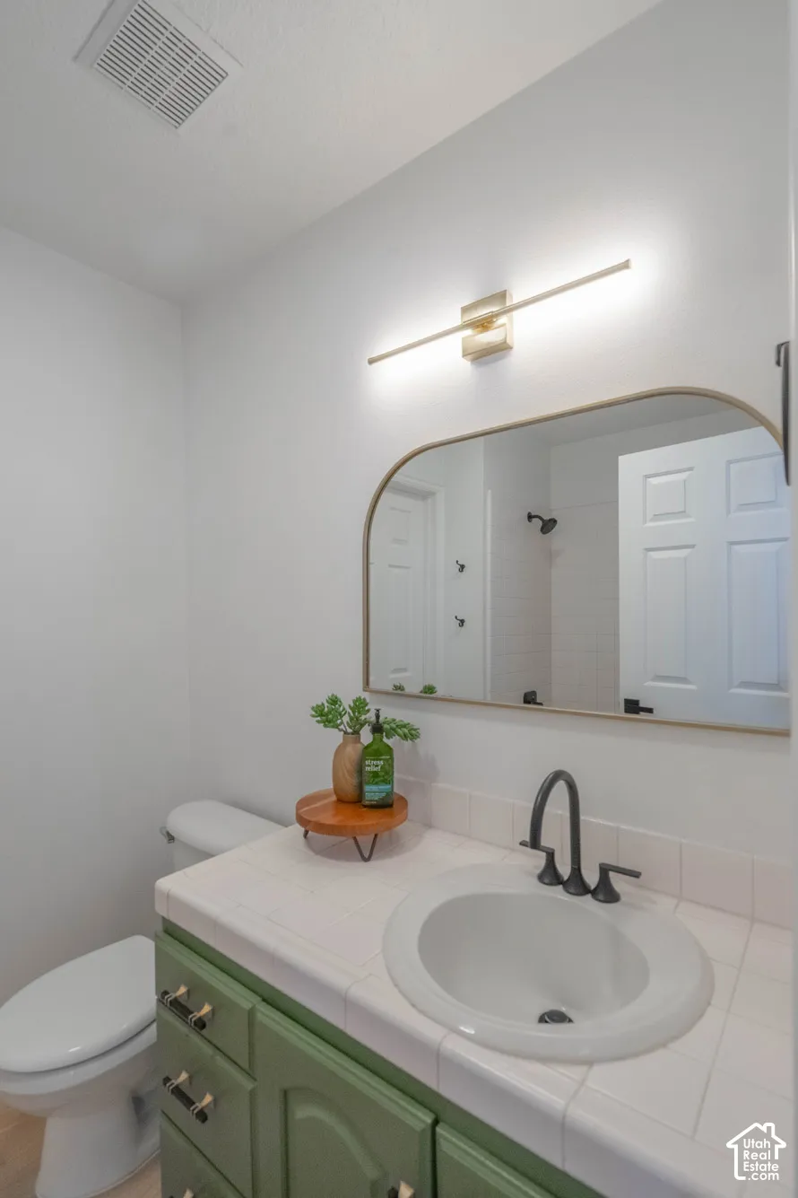 Green vanity cabinetry with dark hardware, white tiled countertop, and an oval undermount sink with a black faucet