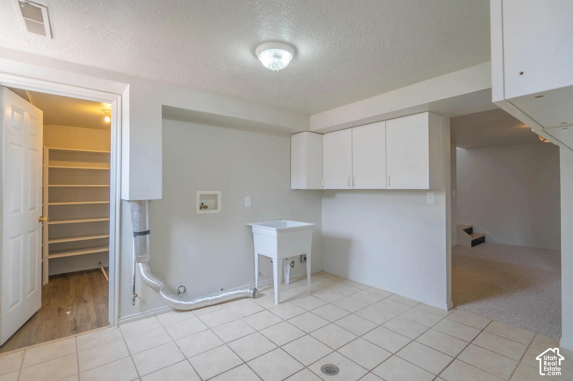 White cabinetry, utility sink, tile flooring, and a separate pantry with built-in shelving
