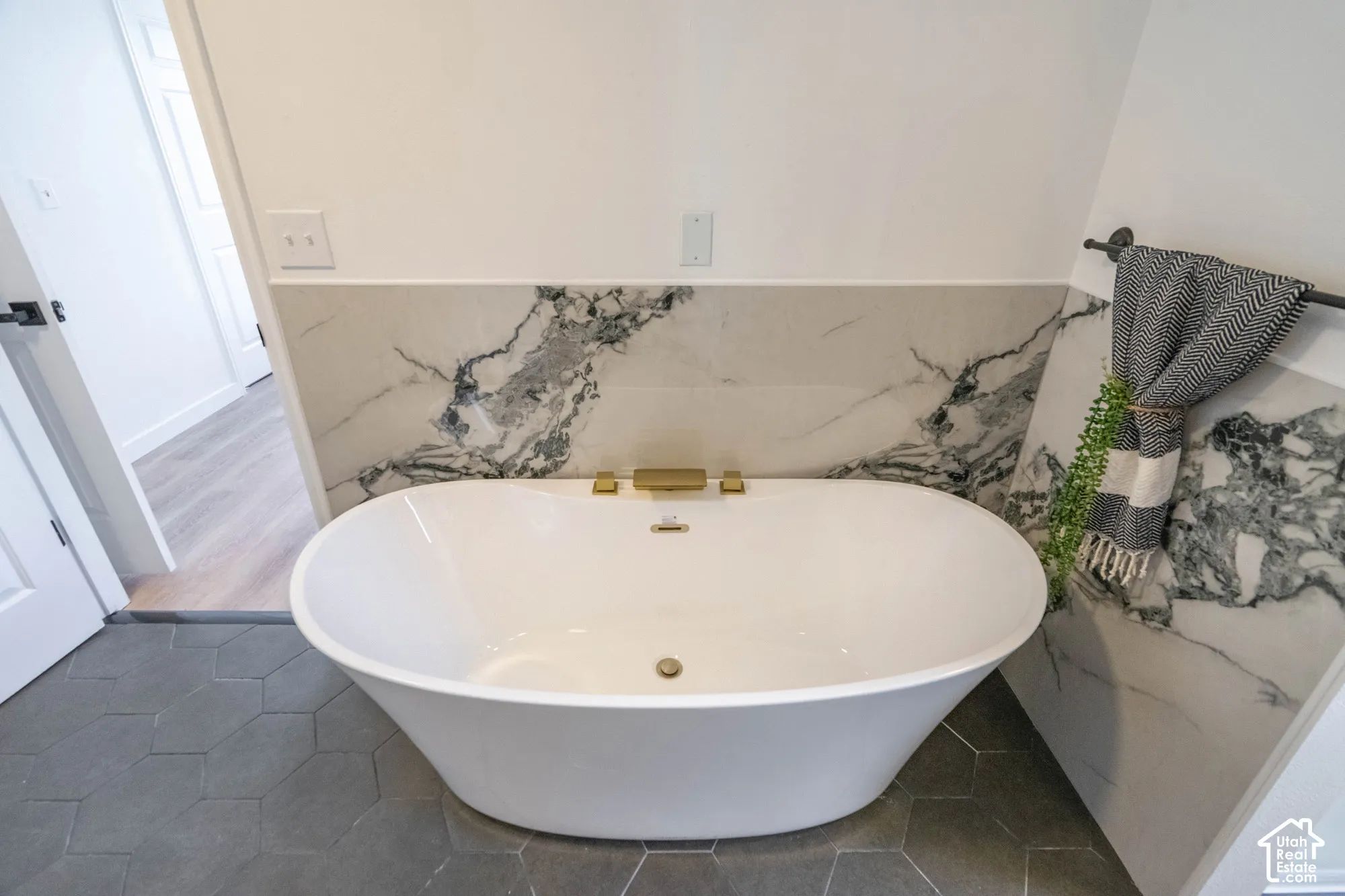 Freestanding soaking tub with gold-finish fixtures, marble-patterned wainscoting, and hexagonal floor tiling