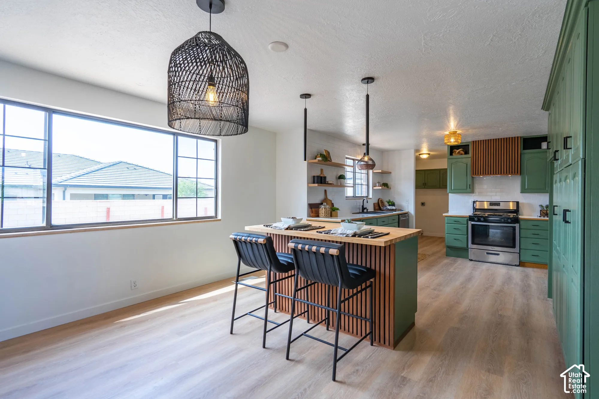 Open-concept kitchen featuring wood-finish flooring, a central island with wood paneling, green cabinetry, stainless steel appliances, and a tiled backsplash
