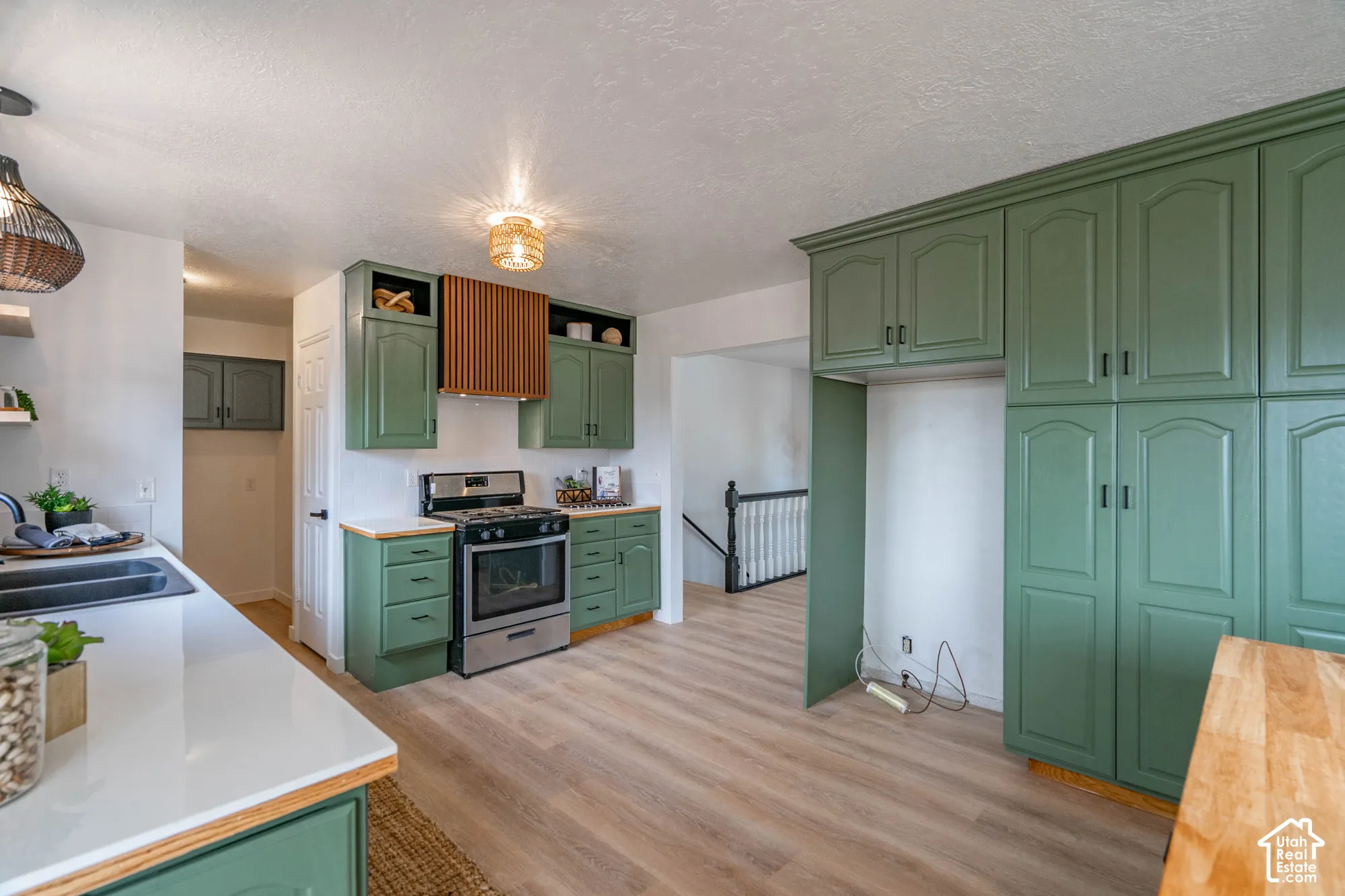 Kitchen featuring extensive green cabinetry, stainless steel range, wood-finish flooring, white countertops, and a decorative range hood