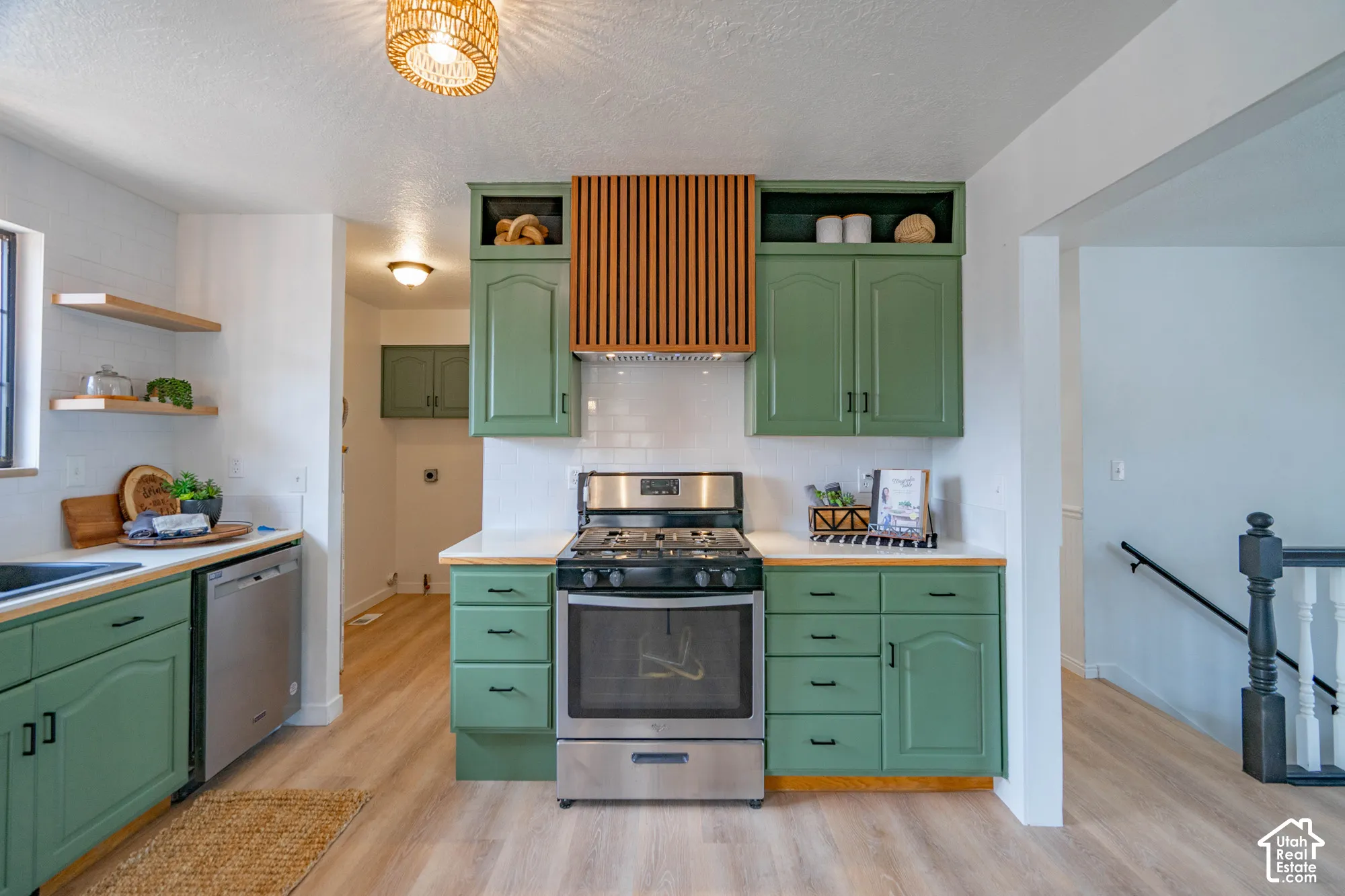 Kitchen featuring sage green cabinetry, stainless steel appliances, wood-finish countertops, subway tile backsplash, and light wood-finish flooring