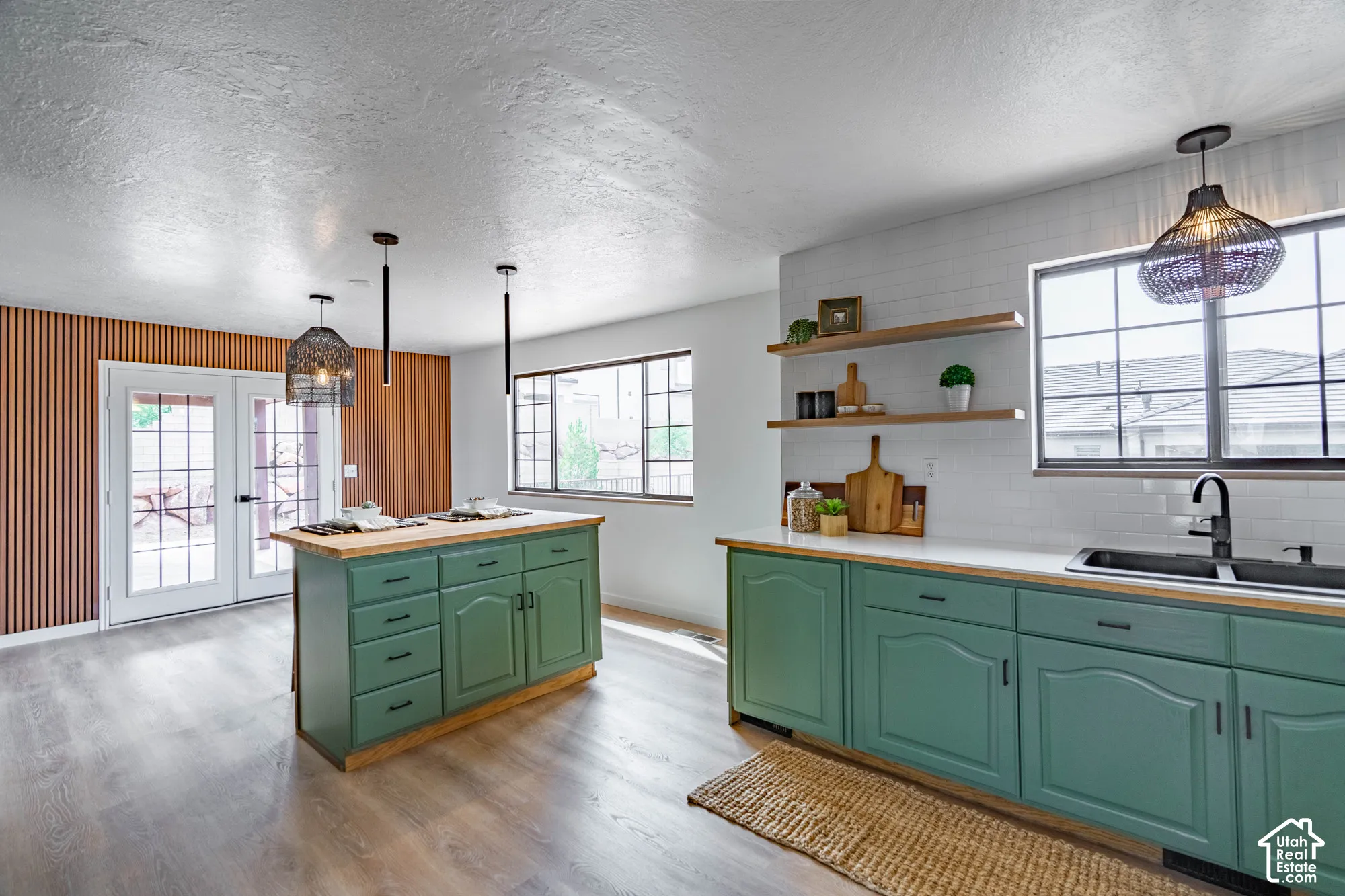 Wood-finish flooring throughout, featuring a kitchen with green cabinetry, white countertops, and a white subway tile backsplash