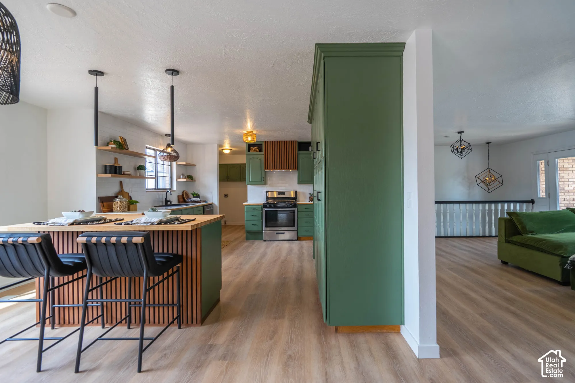 Open-concept kitchen with a breakfast bar, green cabinetry, wood-finish flooring, and pendant lighting