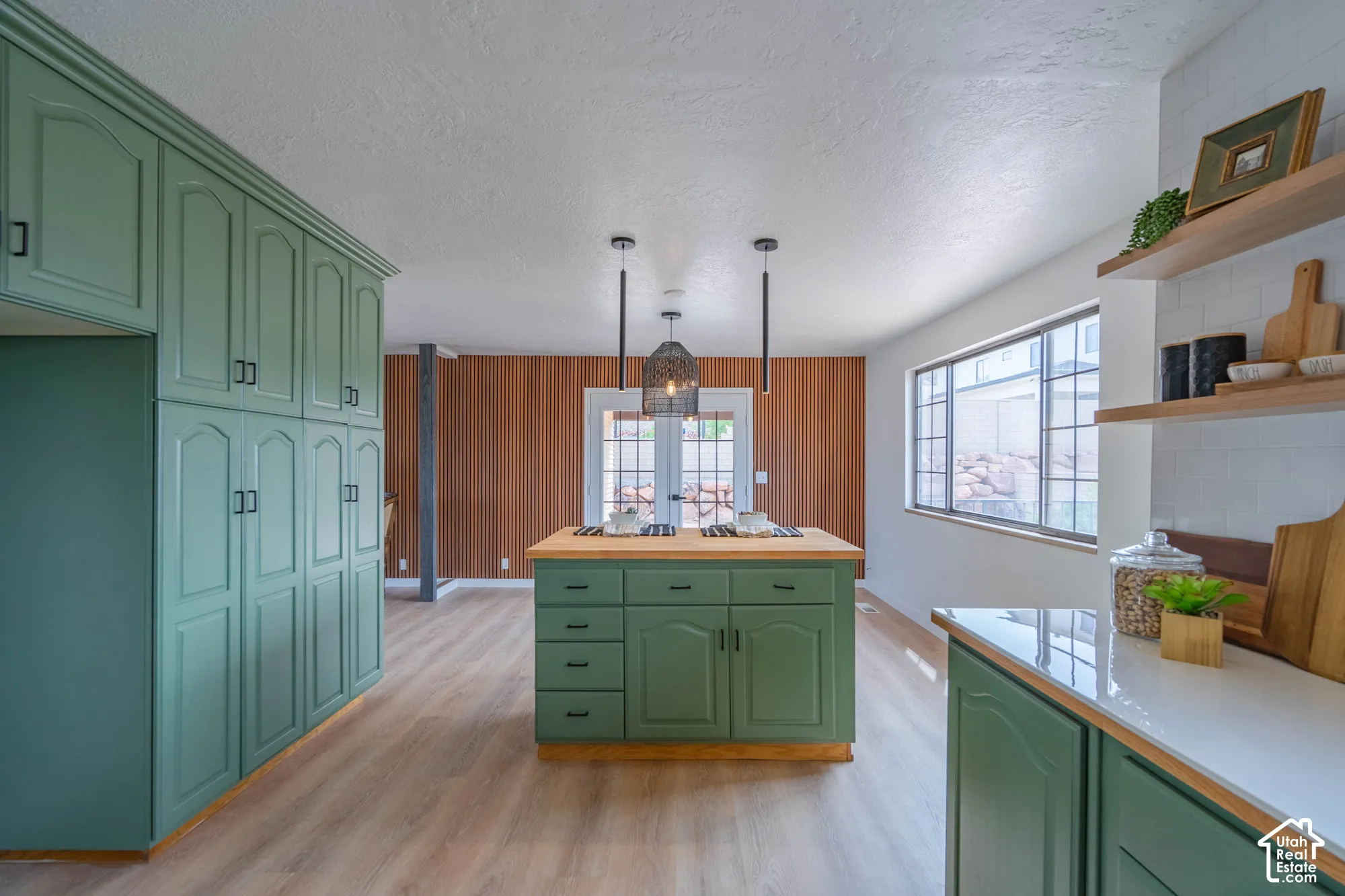 Green cabinetry with black hardware, wood-finish flooring, white countertops, built-in open shelving, and a center island with a wood countertop