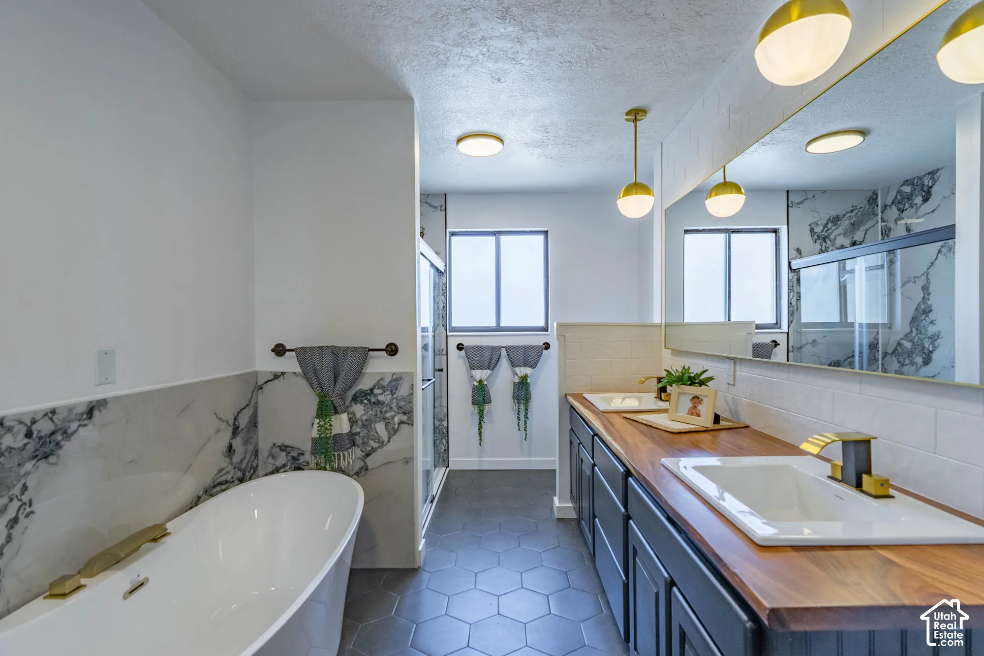 Freestanding soaking tub, dual vanity with wood-finish countertop, hexagon tile flooring, and a glass-enclosed shower