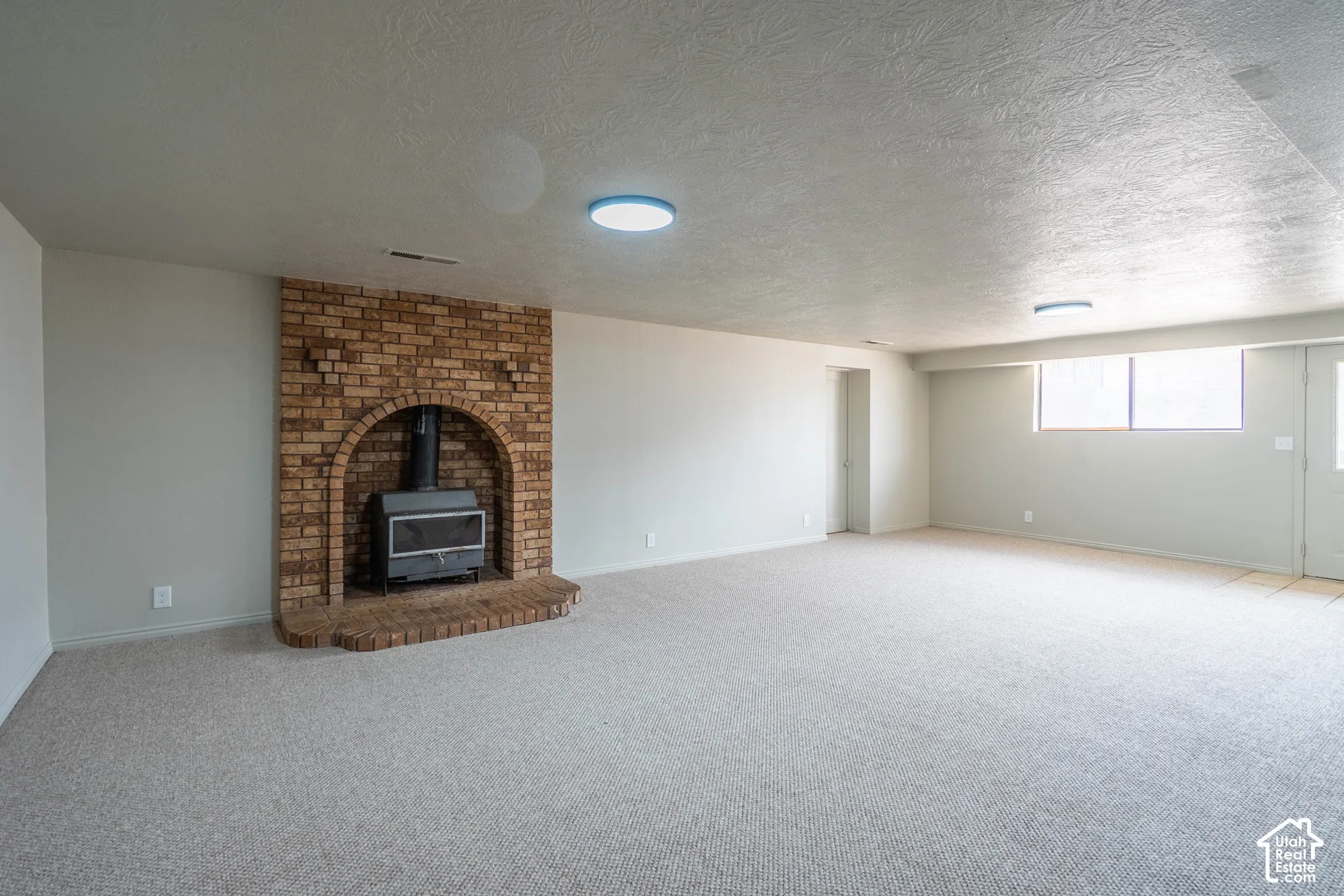 Brick fireplace with a black wood-burning insert, light-toned carpeting, and flush-mount lighting