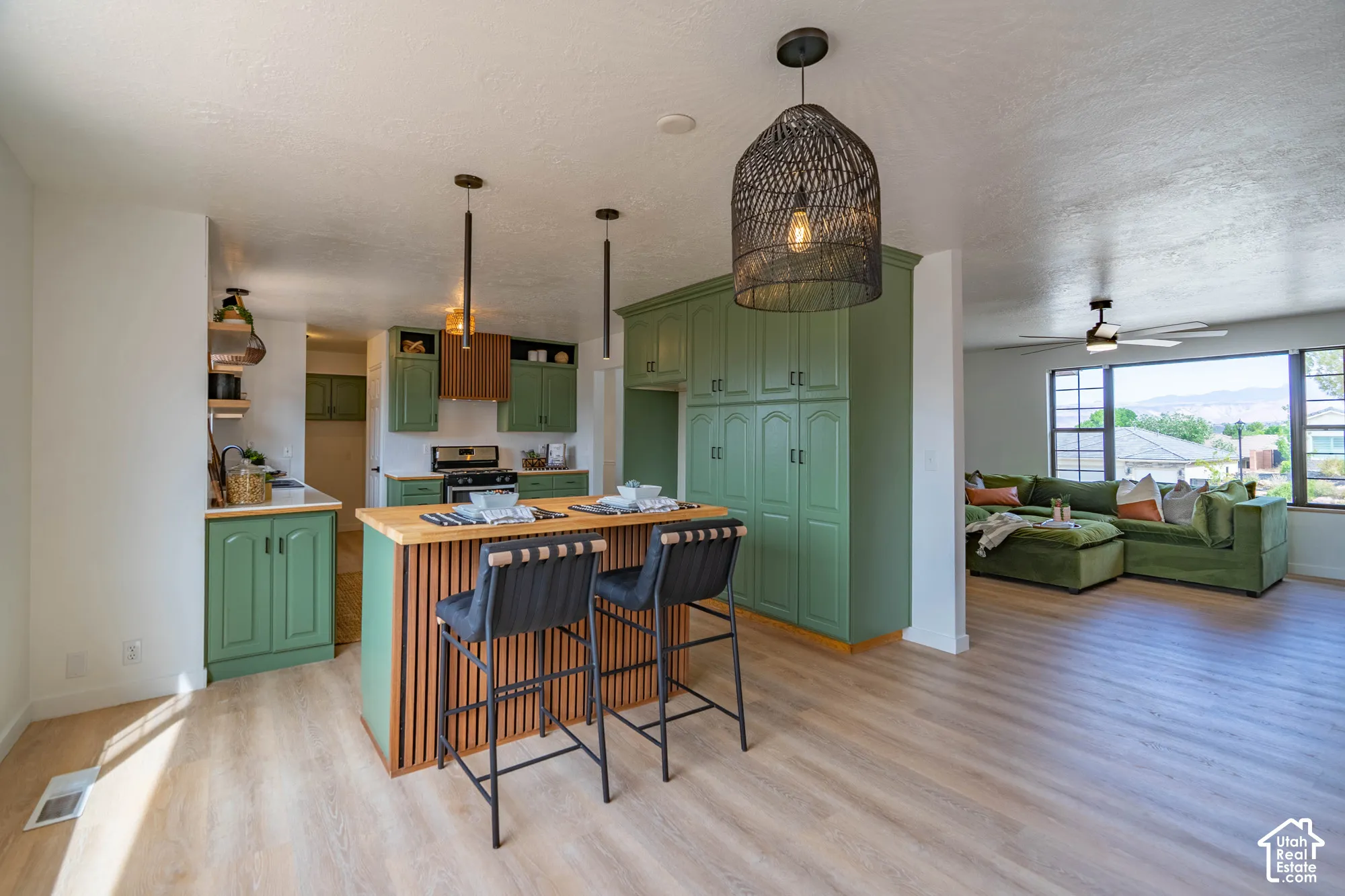 Wood-finish flooring throughout, kitchen with green cabinetry, built-in pantry, island with wood countertop, and modern pendant lighting