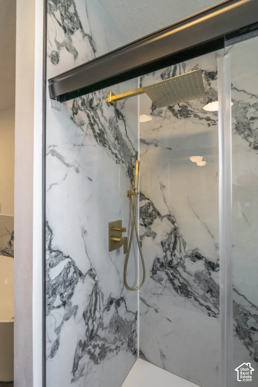 Shower enclosure featuring marble-patterned wall panels, gold-toned fixtures, a built-in shower bench, and a glass shower door with a dark-toned frame