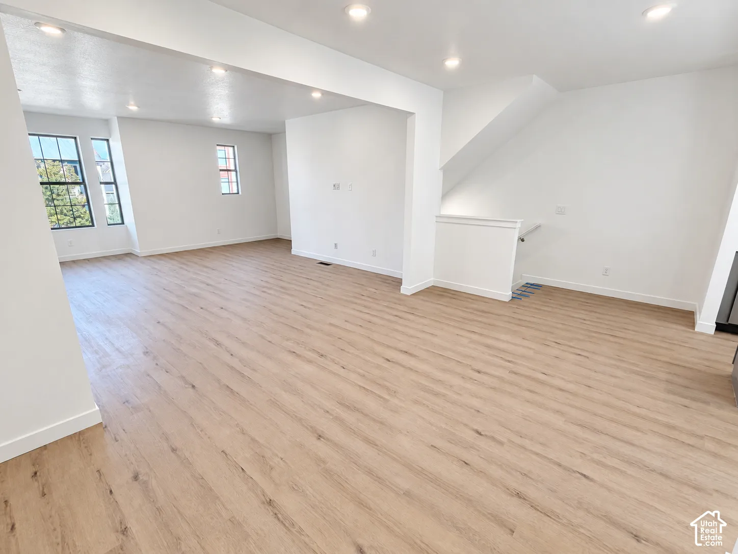 Open-concept interior featuring light wood-finish flooring, recessed lighting, and large windows with black frames