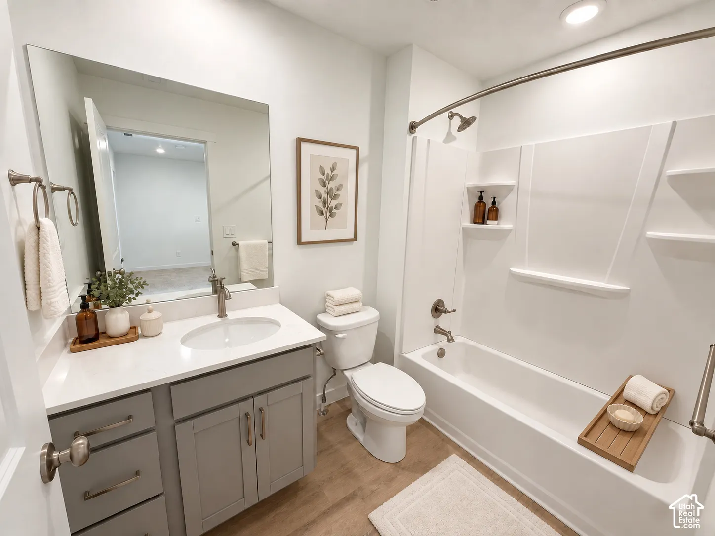 Full-width vanity with white solid-surface countertop and integrated oval sink, gray shaker-style cabinetry, large wall-mounted mirror, and combination tub and shower with built-in shelving