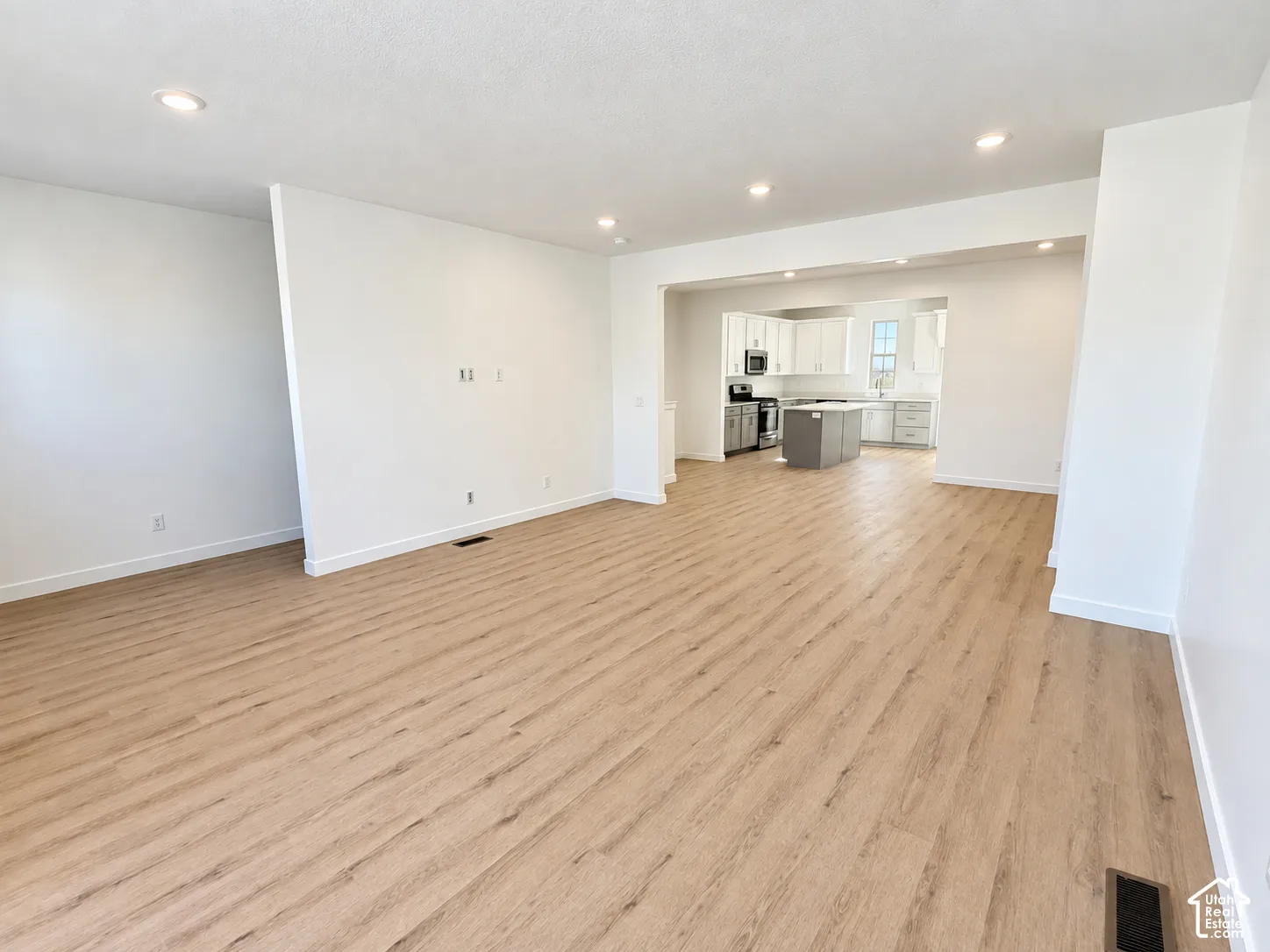 Open-concept interior featuring light wood-finish flooring, recessed lighting, and a kitchen equipped with white cabinetry and a contrasting center island