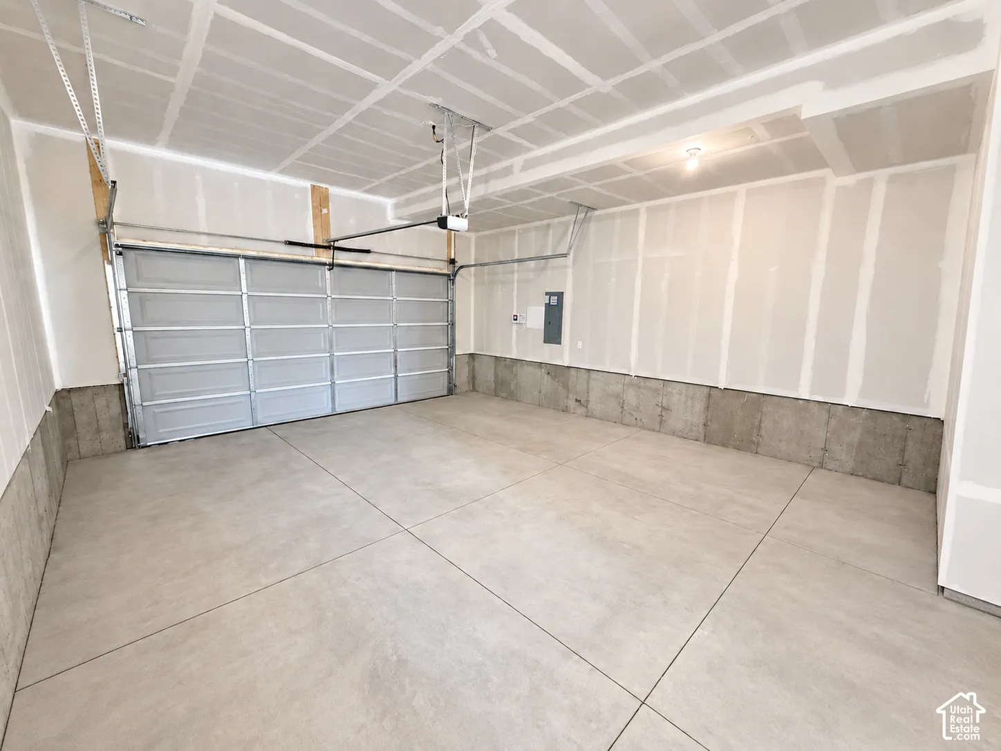 Attached garage featuring concrete flooring, taped drywall, metal sectional overhead door, and automated door opener system