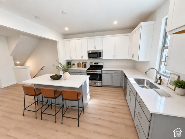 Kitchen featuring white upper cabinetry, grey lower cabinetry, white stone-finish countertops, stainless steel appliances, and a central island with integrated seating