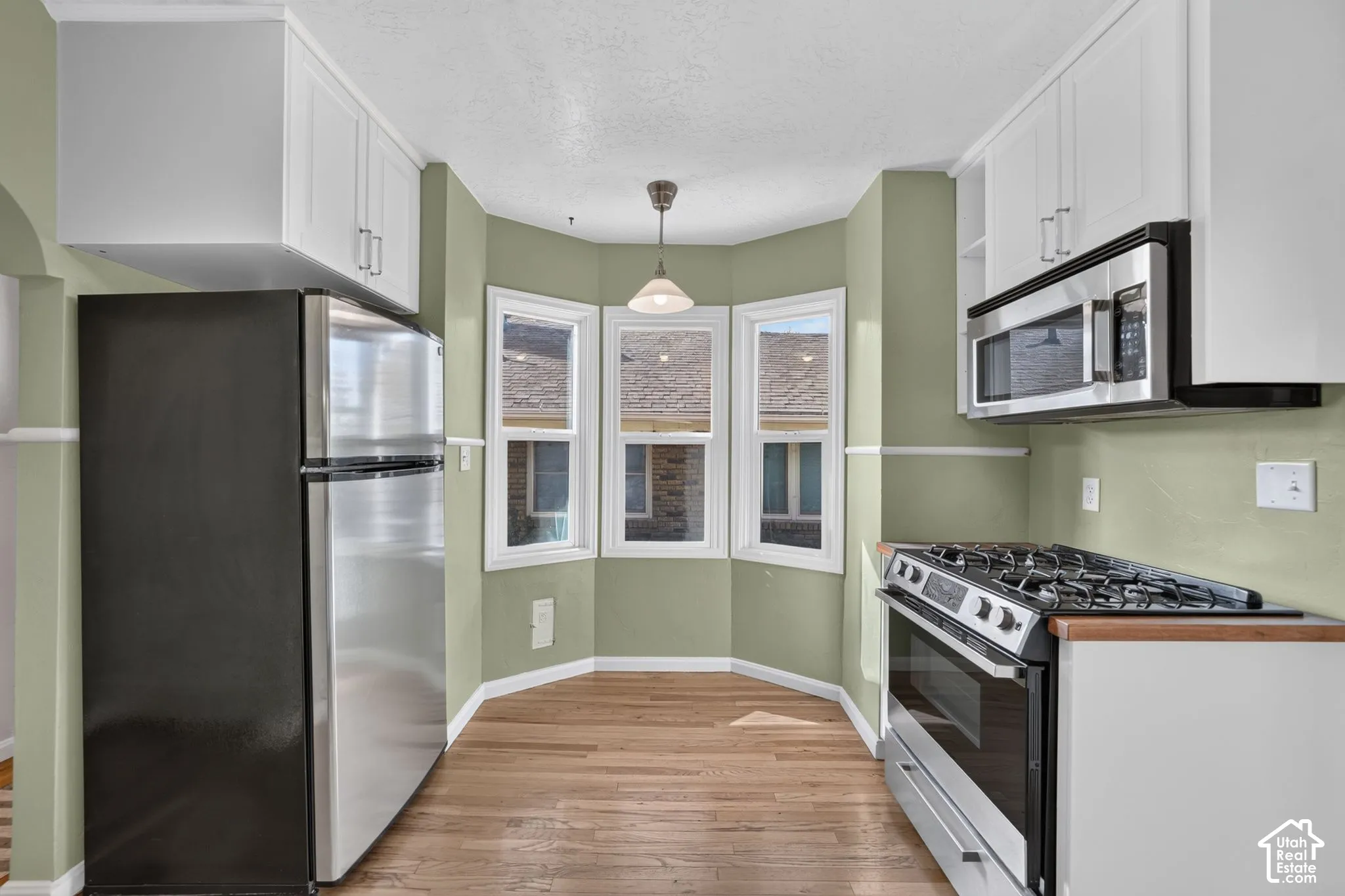 Kitchen featuring stainless steel appliances, white cabinetry, bay window, pendant lighting, and wood-finish flooring