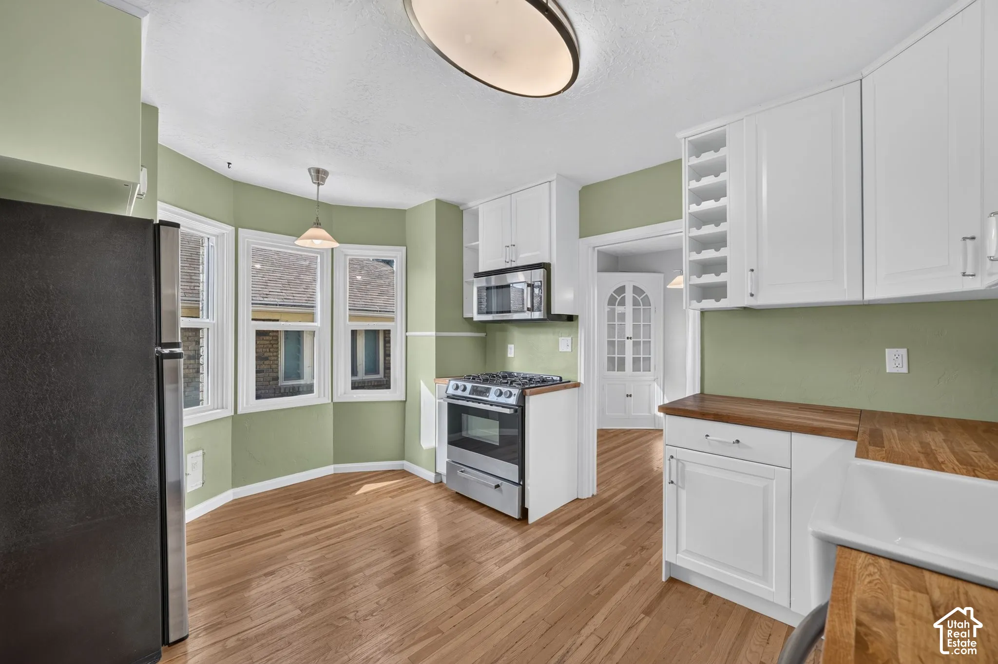 Kitchen featuring wood-finish flooring, butcher block countertops, white shaker-style cabinetry with built-in wine storage, stainless steel appliances, and a bay window