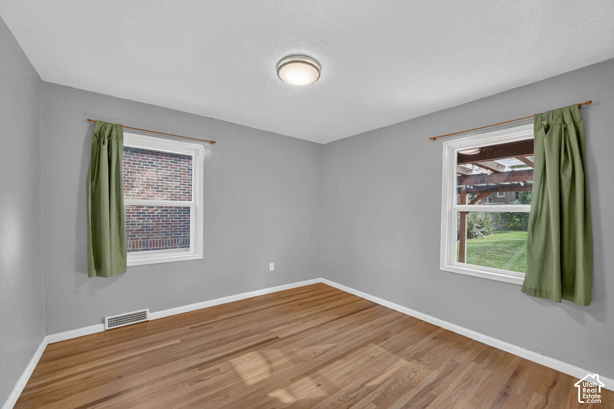 Room featuring wood-finish flooring, dual windows with white casings, and a central flush-mount ceiling light fixture