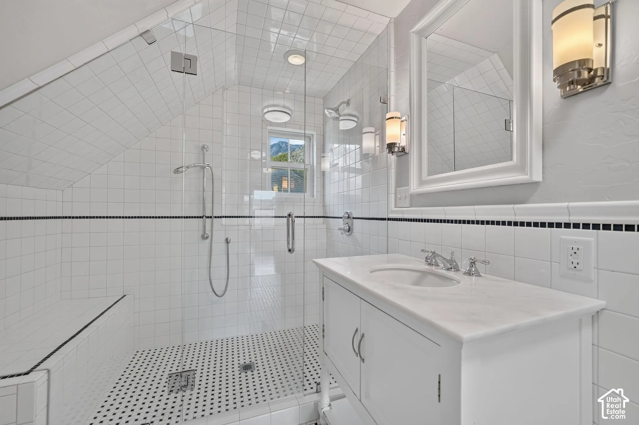 Bathroom featuring a white vanity with a stone countertop, a walk-in glass shower enclosure with white tile walls and a built-in bench, and black-and-white mosaic tile flooring