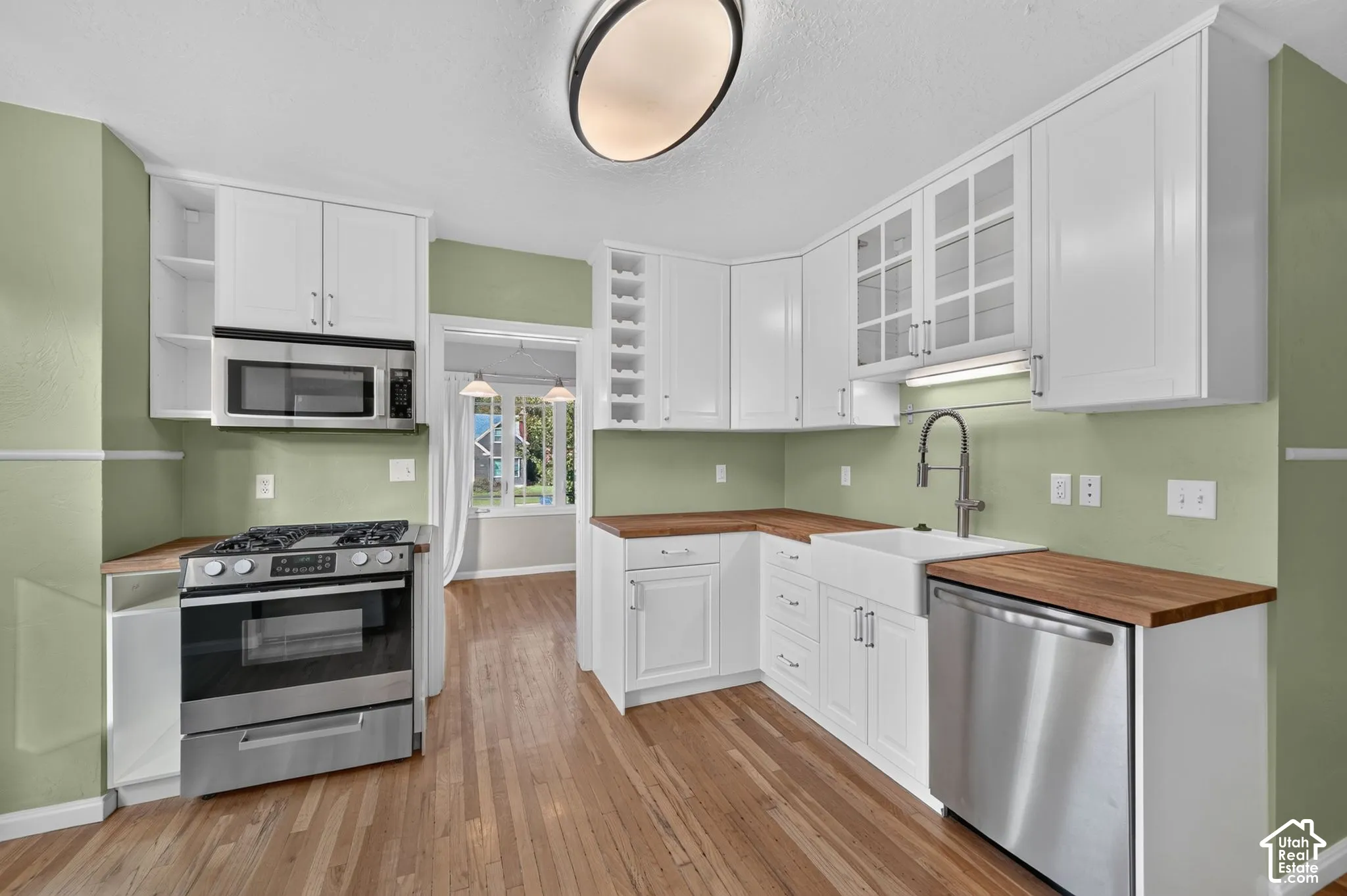 Kitchen featuring white shaker-style cabinetry with built-in wine storage, wood-finish countertops, stainless steel appliances, apron-front sink with gooseneck faucet, and wood-finish flooring