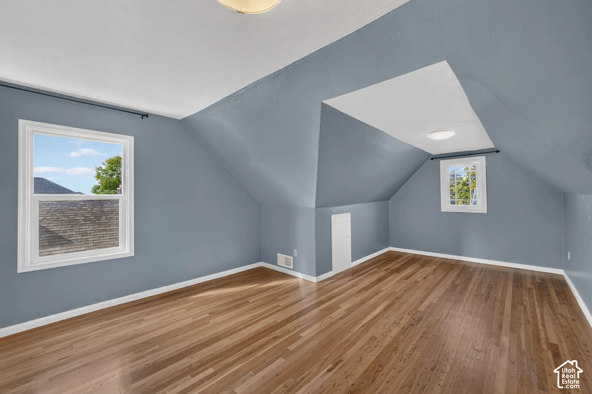 Finished room featuring vaulted ceilings, wood-finish flooring, dual windows, and built-in knee-wall storage