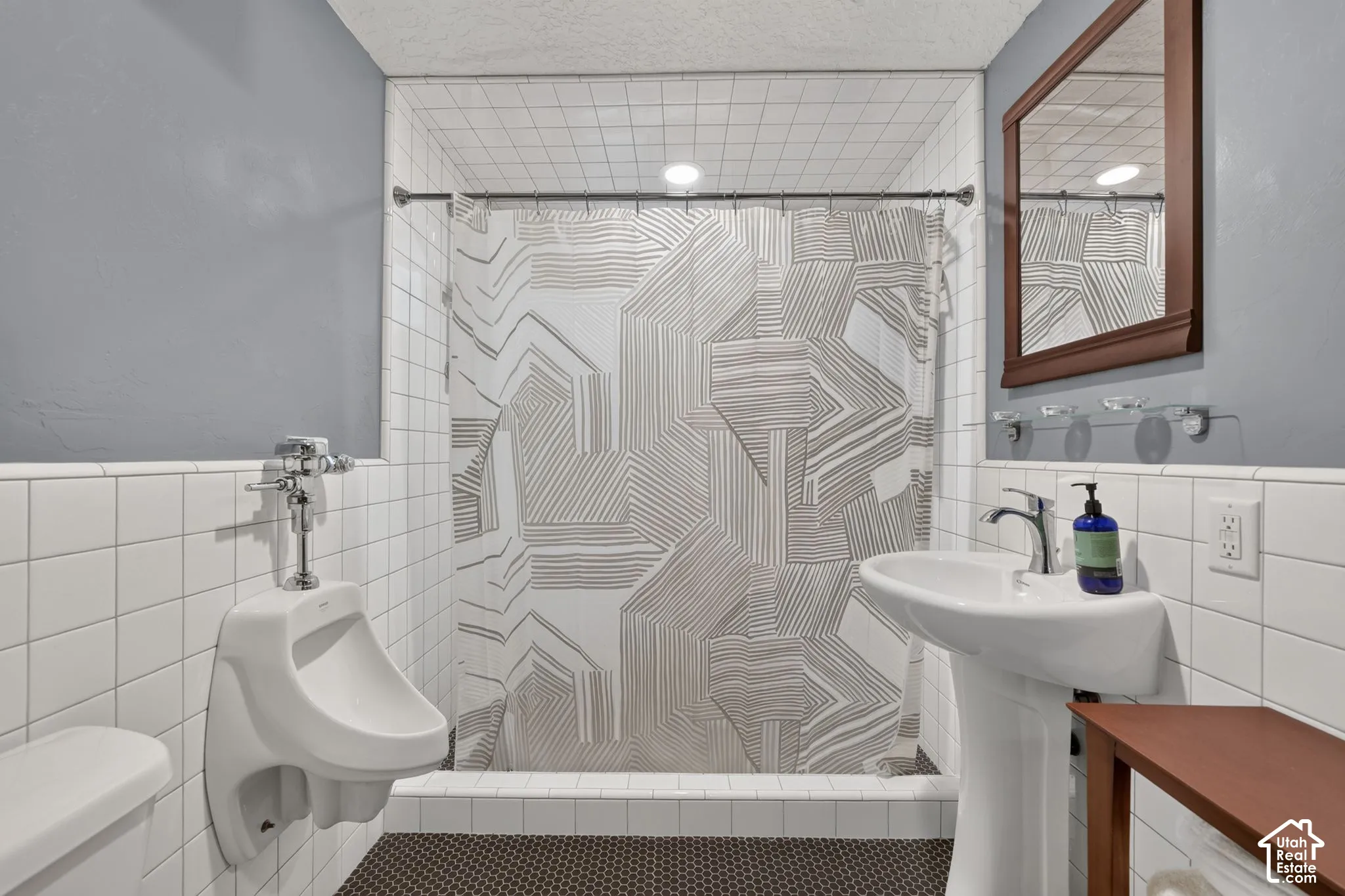 Bathroom featuring white square wall tile, a wall-mounted urinal, a white pedestal sink with a chrome faucet, and a shower area with a ceiling-mounted light fixture