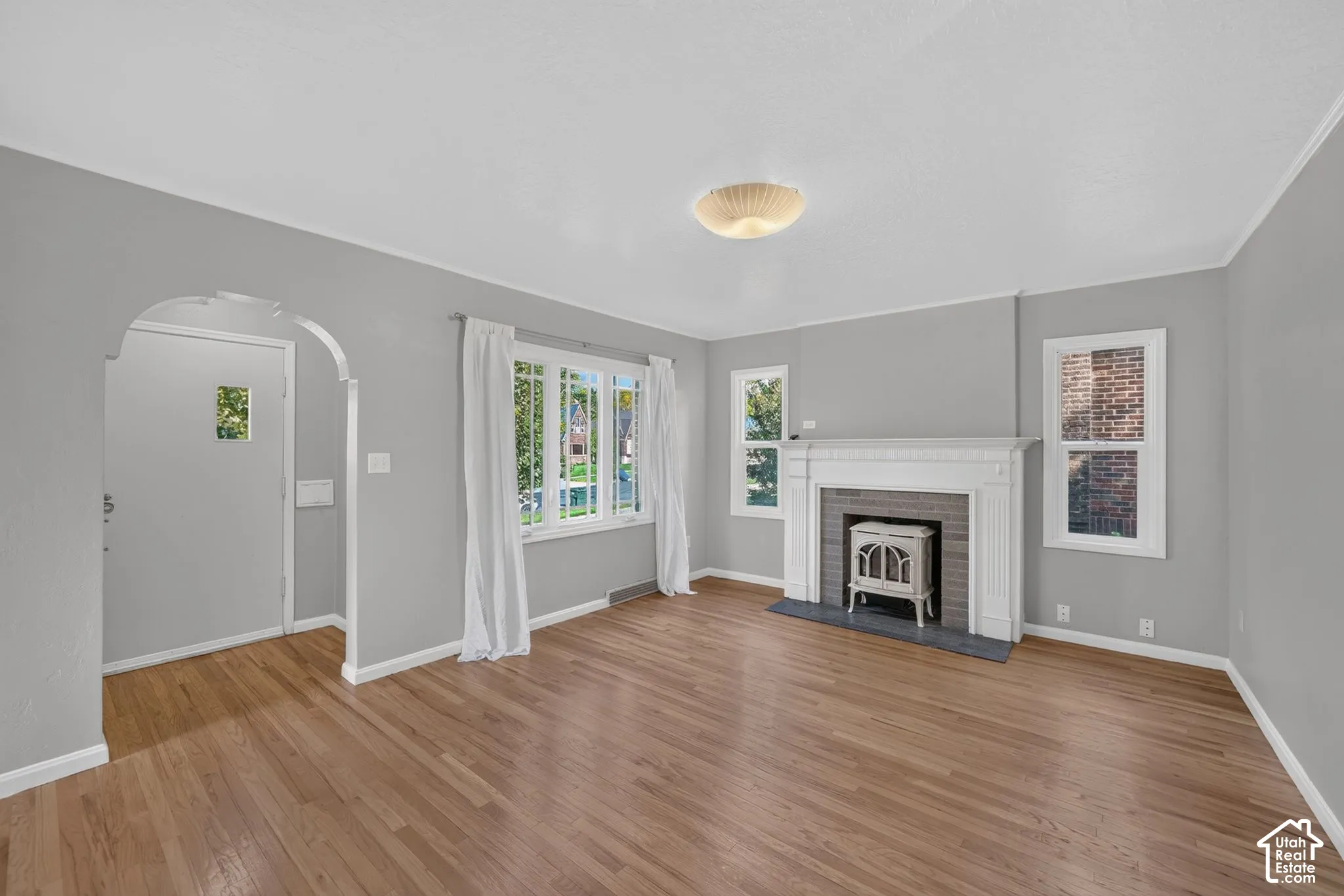 Hardwood flooring, arched entryway, fireplace with white mantel and tile surround, and large windows