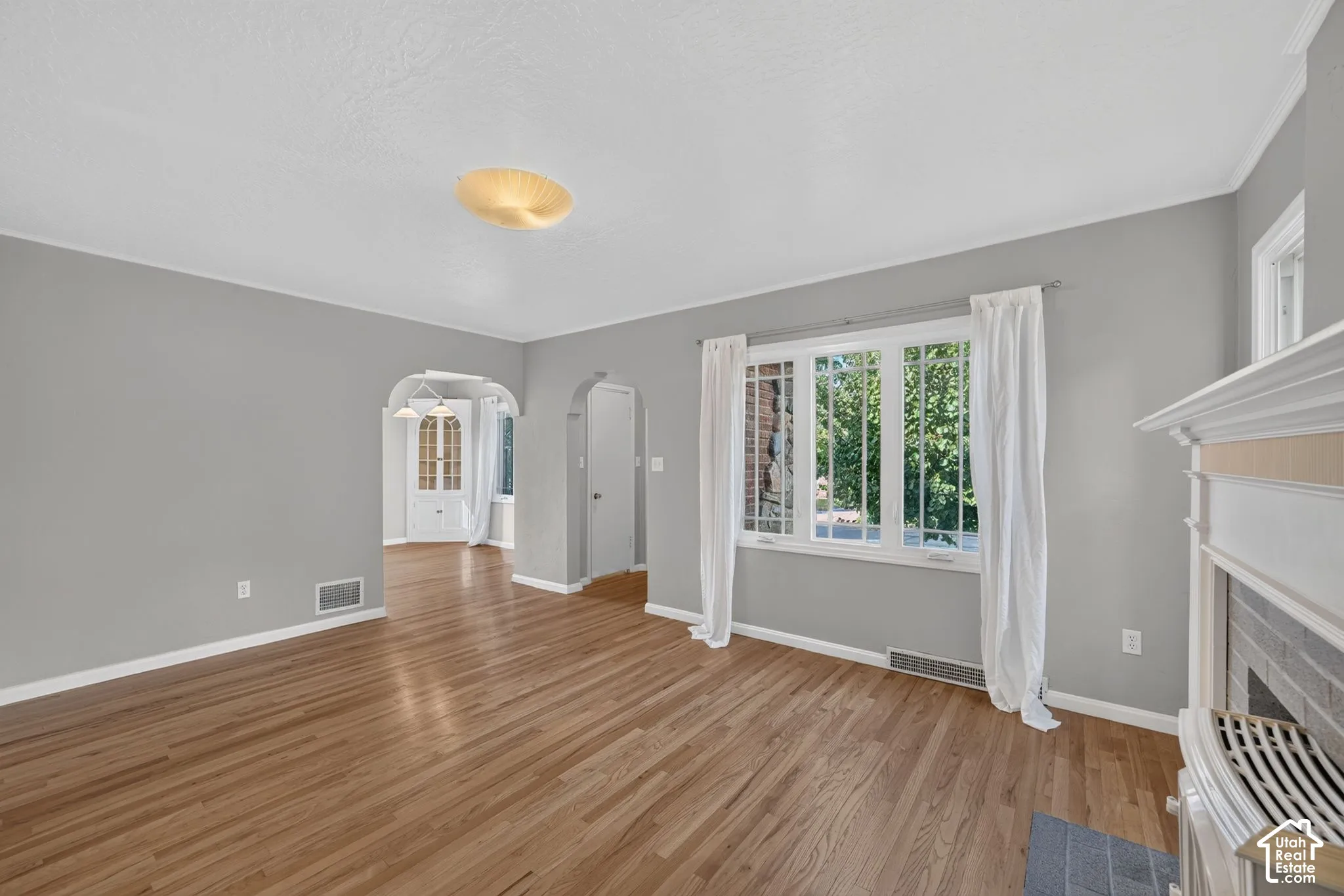 Living area featuring wood-finish flooring, multi-pane window, arched doorways, and a fireplace with a mantel