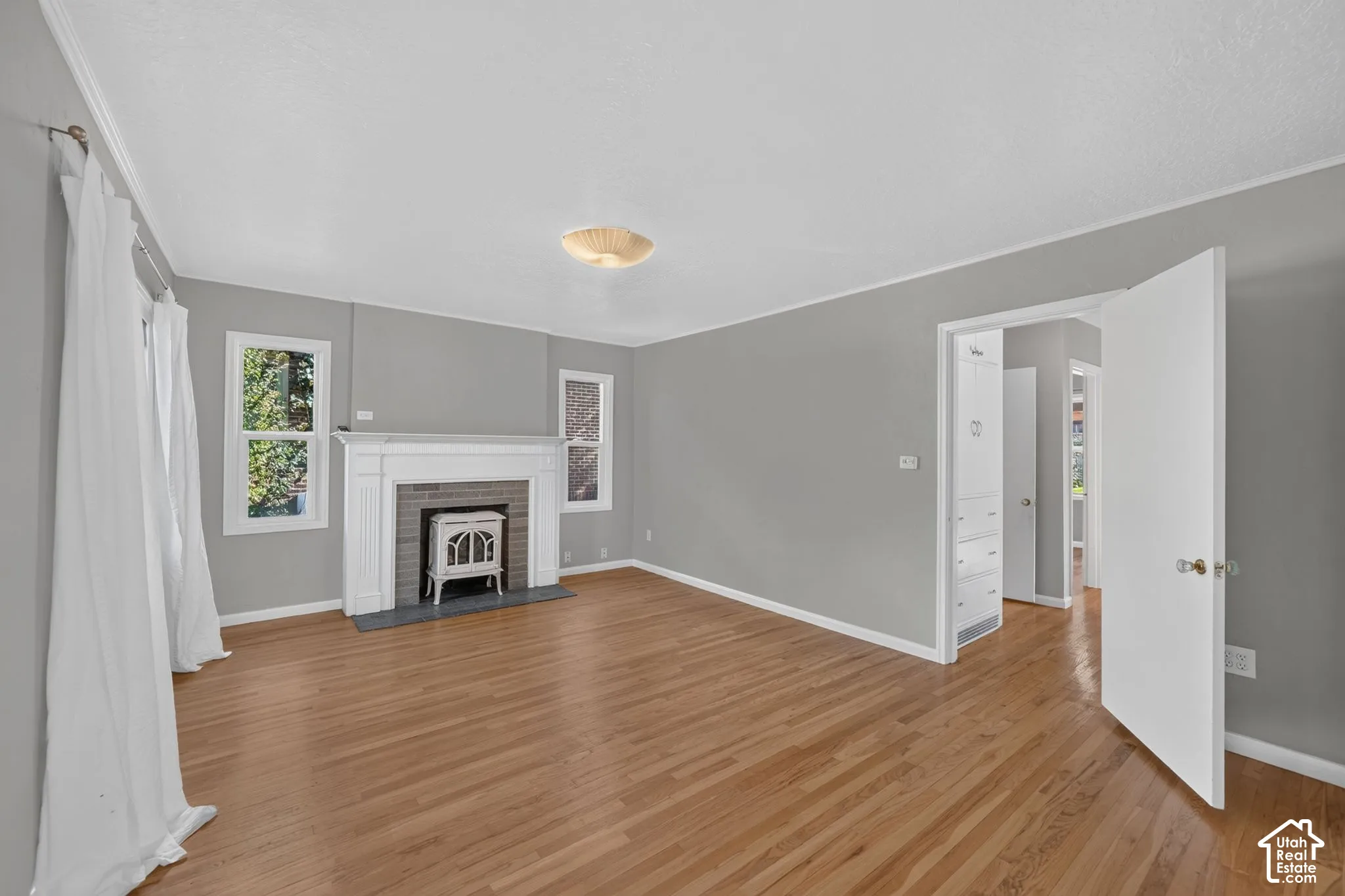 Living area featuring wood-finish flooring, a fireplace with a white mantel and brick surround, a metal stove insert, and built-in cabinetry