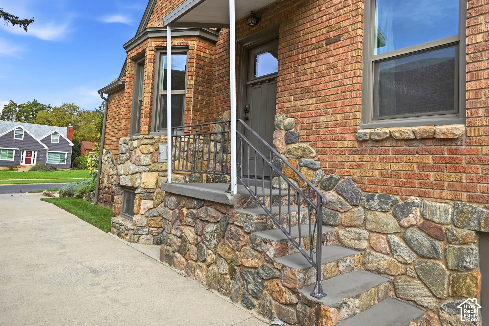 Exterior facade featuring a brick finish, fieldstone accents, concrete steps with metal railings, and a concrete driveway