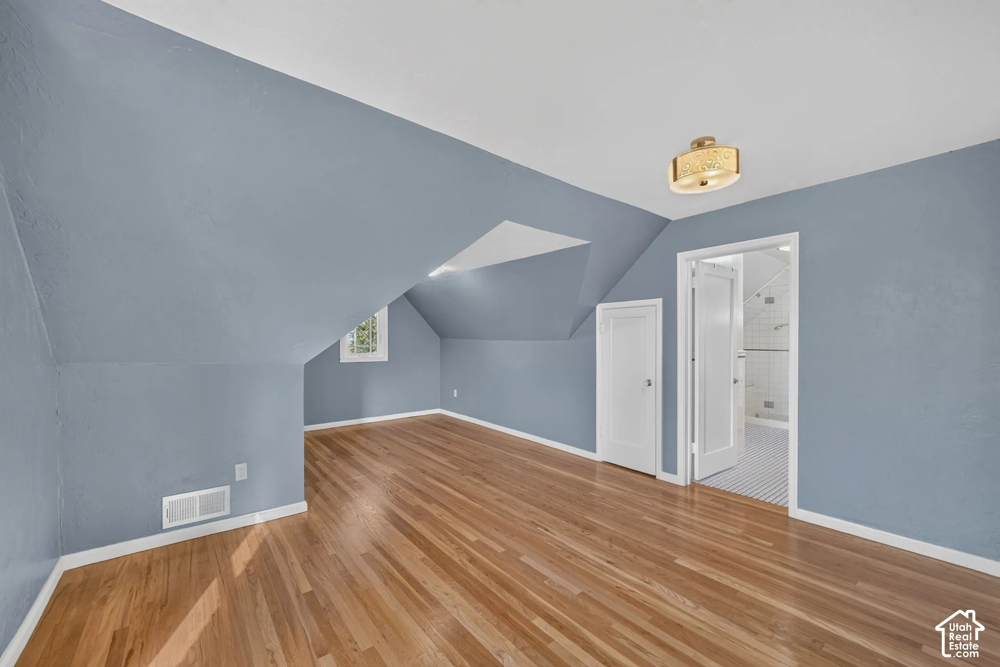 Room featuring wood-finish flooring, vaulted ceilings with architectural angles, flush-mount circular lighting, and a white interior door