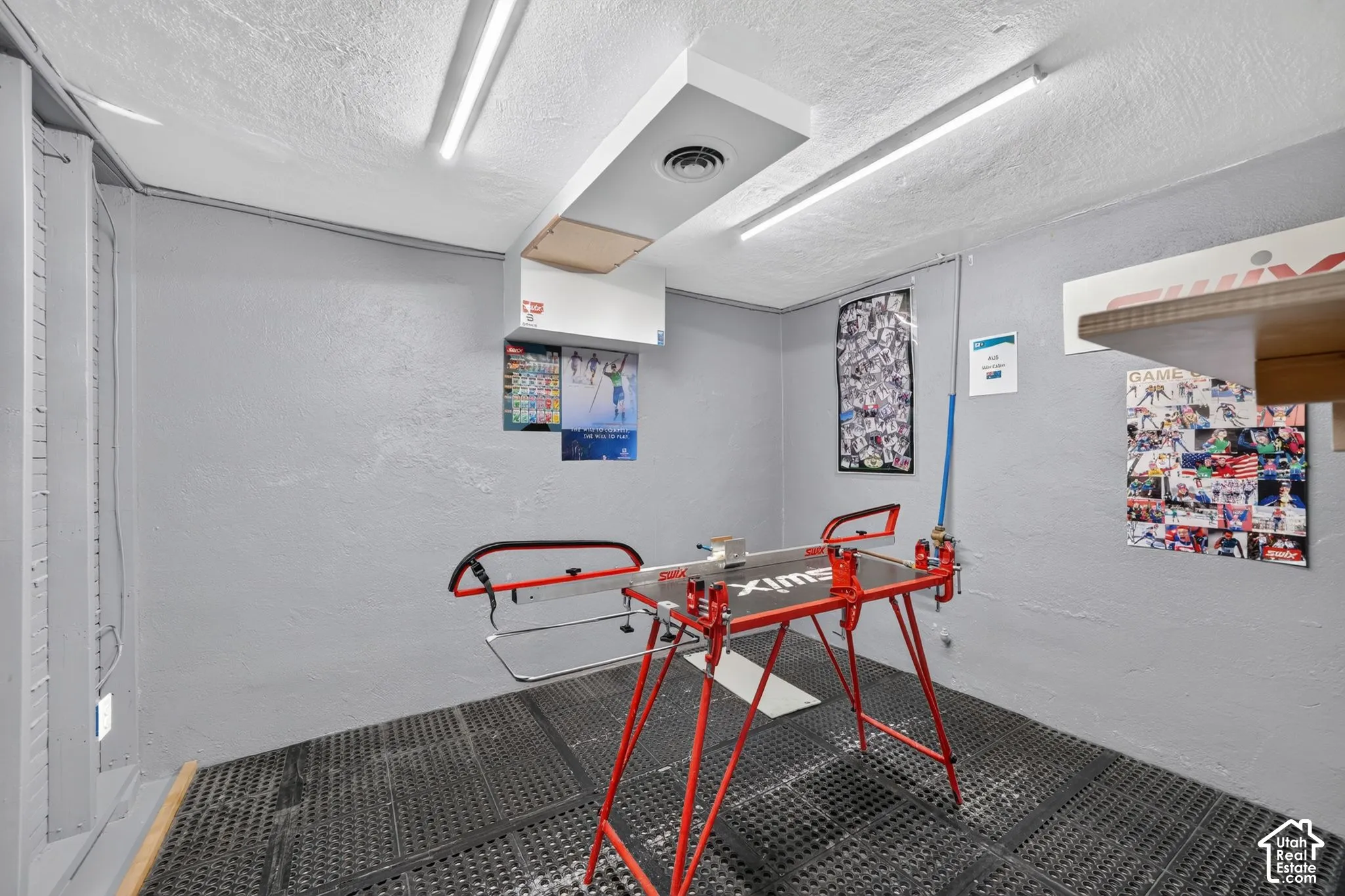 Dedicated utility area featuring textured walls, industrial-style rubberized flooring, integrated ceiling-mounted linear lighting, and a centralized HVAC duct system