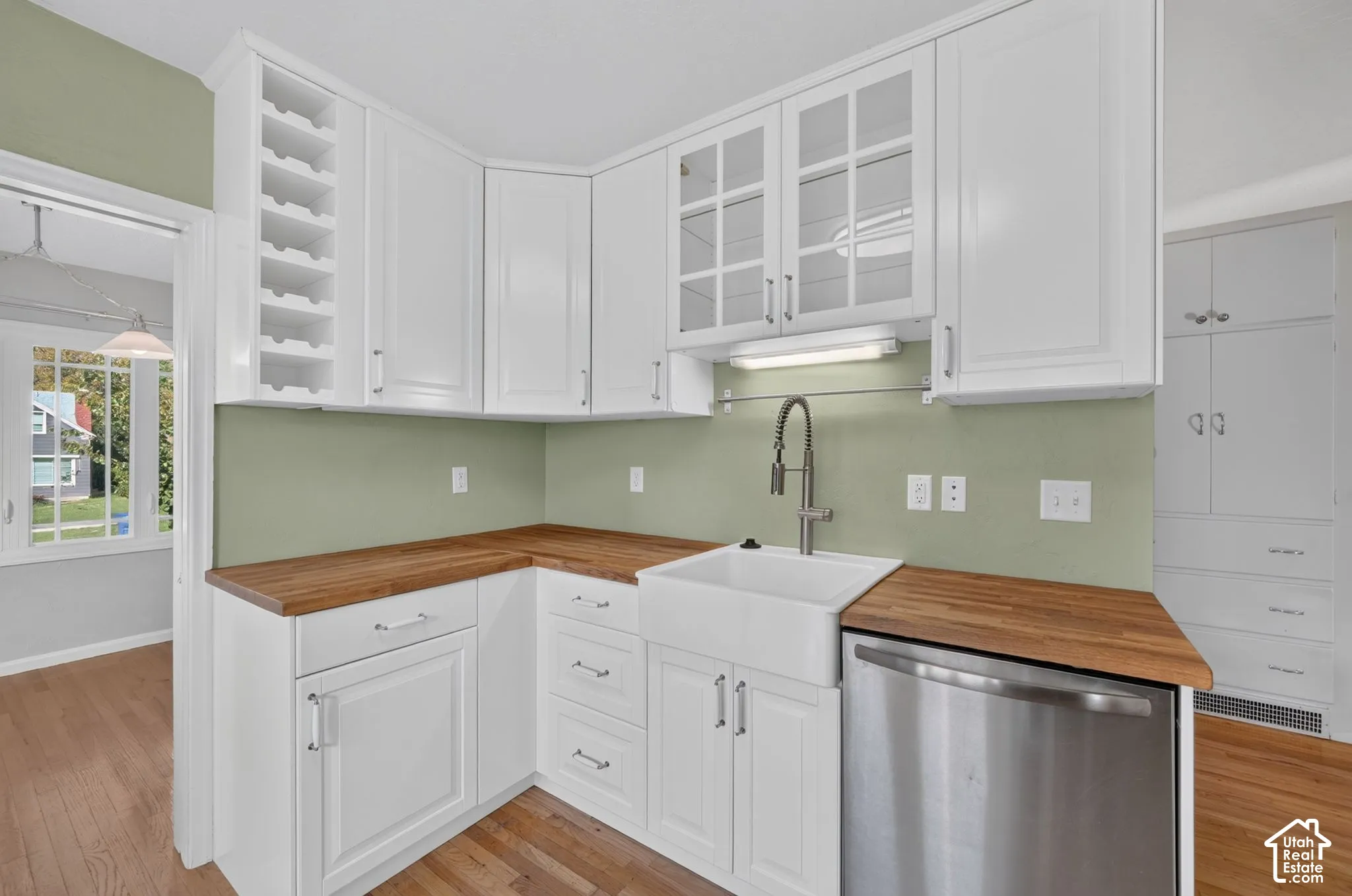 White shaker cabinetry with built-in wine rack, wood-finish countertops, ceramic farmhouse sink with pull-down faucet, and glass-front upper cabinets
