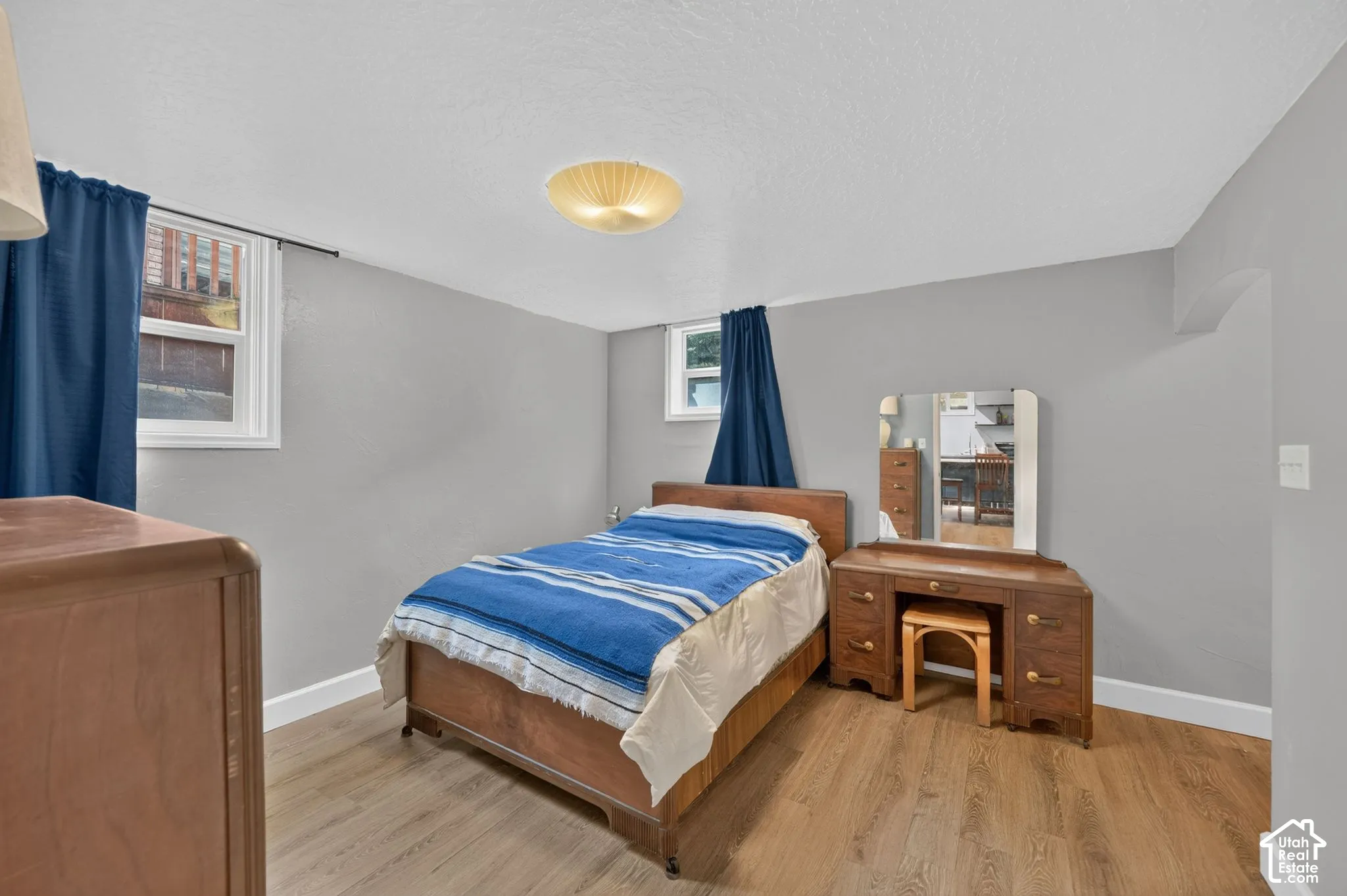 Neutral-toned interior space featuring wood-finish flooring, two windows with white trim, and a flush-mount dome light fixture