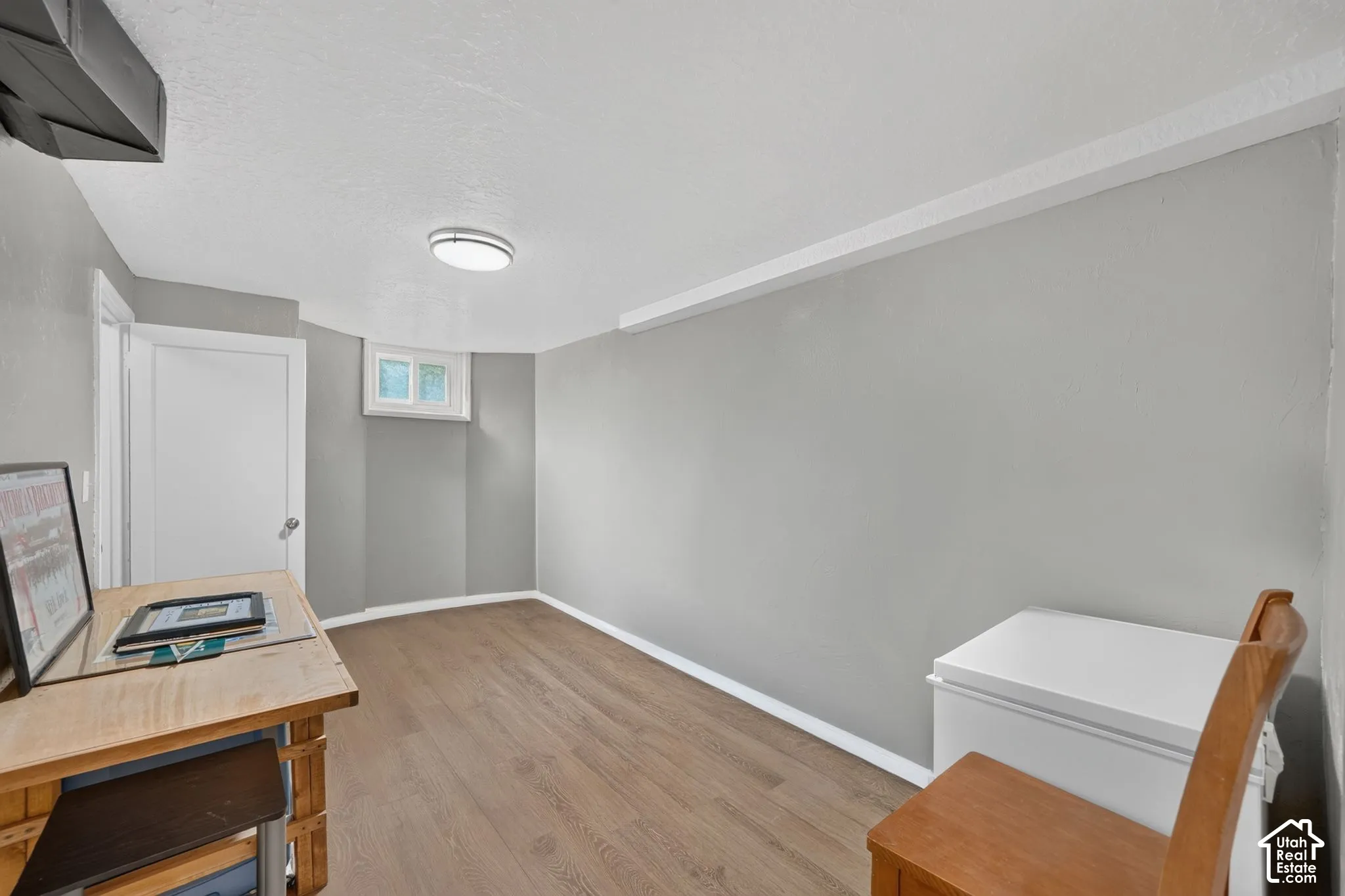 Interior room featuring neutral gray wall paint, wood-finish flooring, a flush-mount ceiling light fixture, and a single recessed window