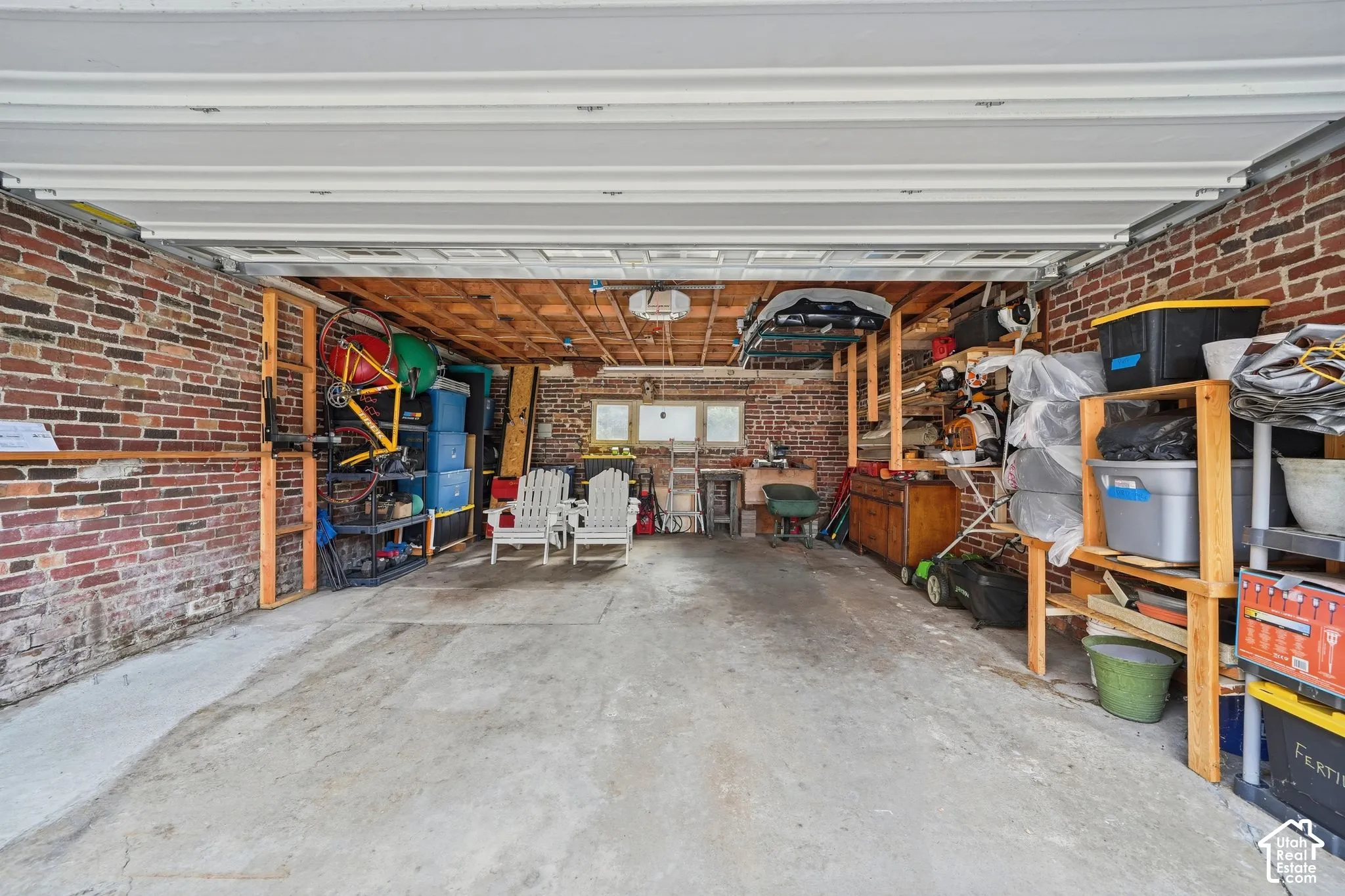 Two-car garage featuring exposed brick walls, concrete flooring, overhead garage door system, and timber-framed ceiling structure