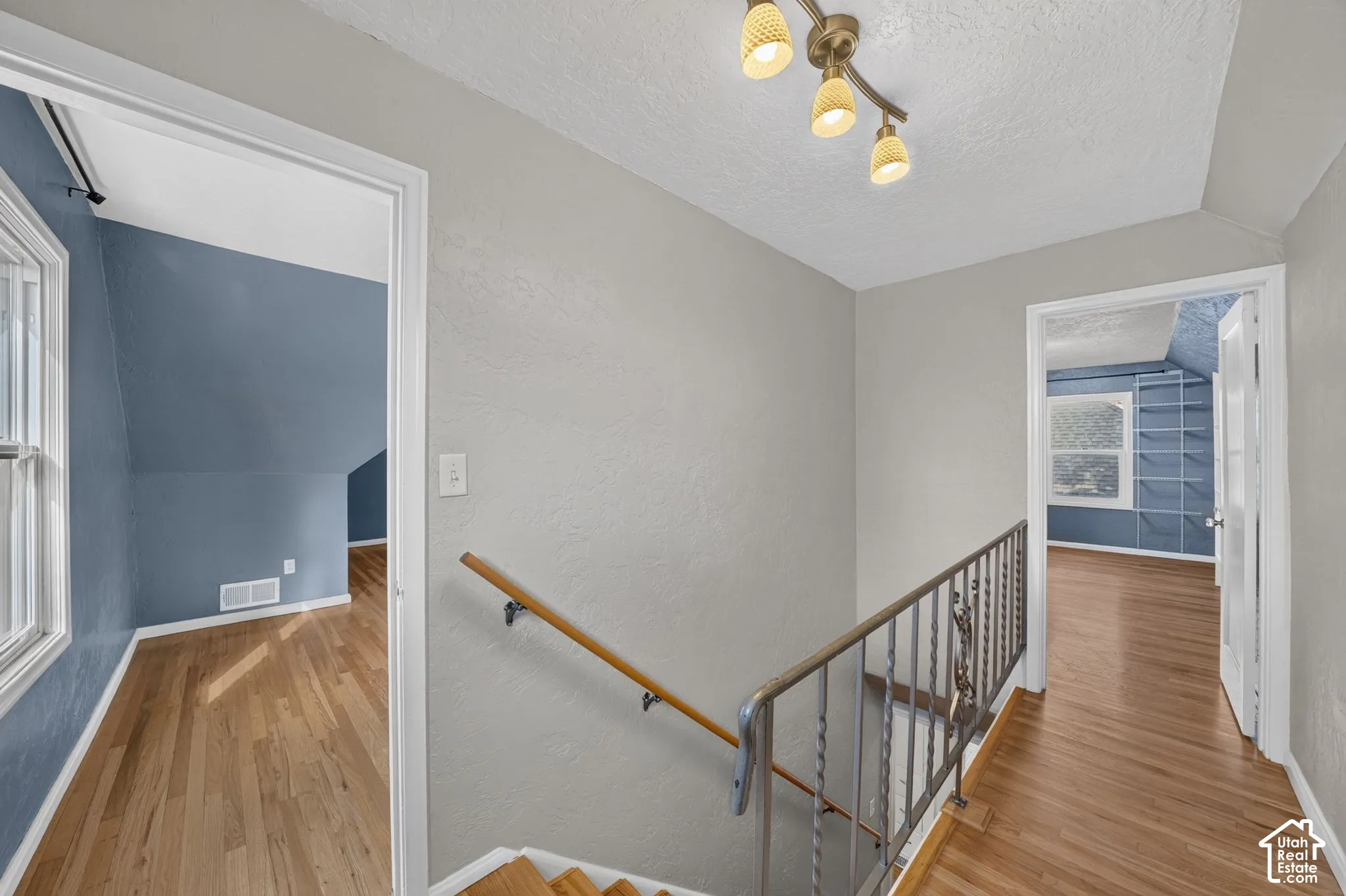 Hallway featuring wood-finish flooring, metal staircase railing with wooden handrail, multi-bulb track lighting, and built-in shelving