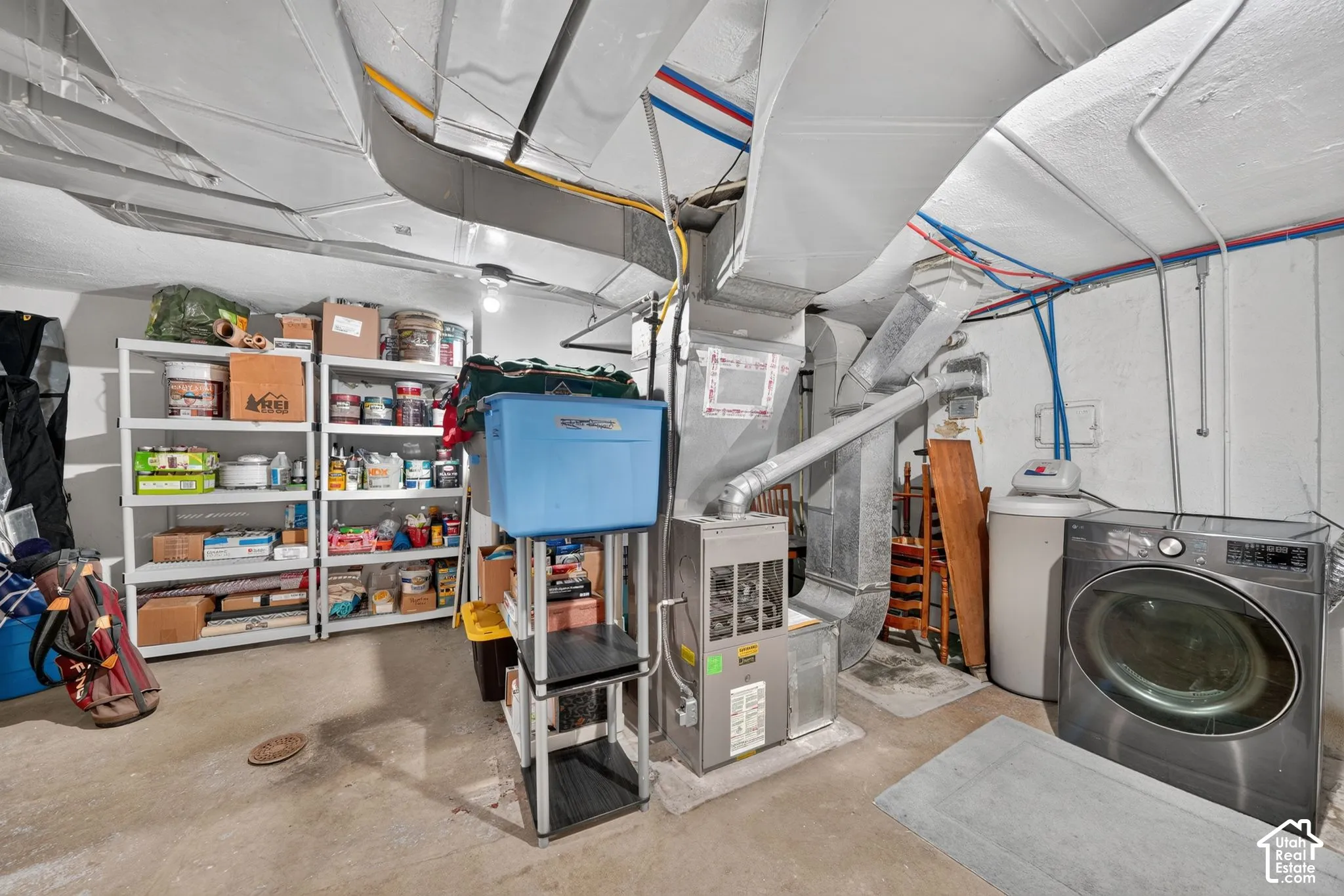 Utility area featuring a central furnace, water softener, and front-loading washing machine, complemented by white painted masonry walls and concrete flooring