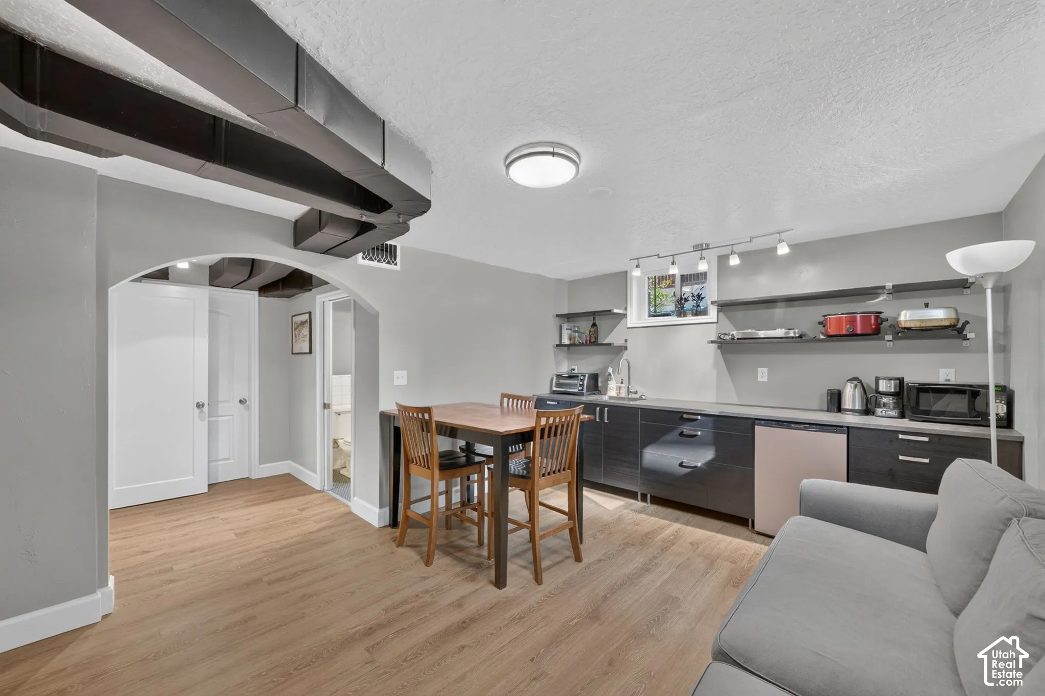 Kitchenette featuring dark cabinetry, solid-surface countertops, built-in under-counter refrigerator, open shelving, and wood-finish flooring