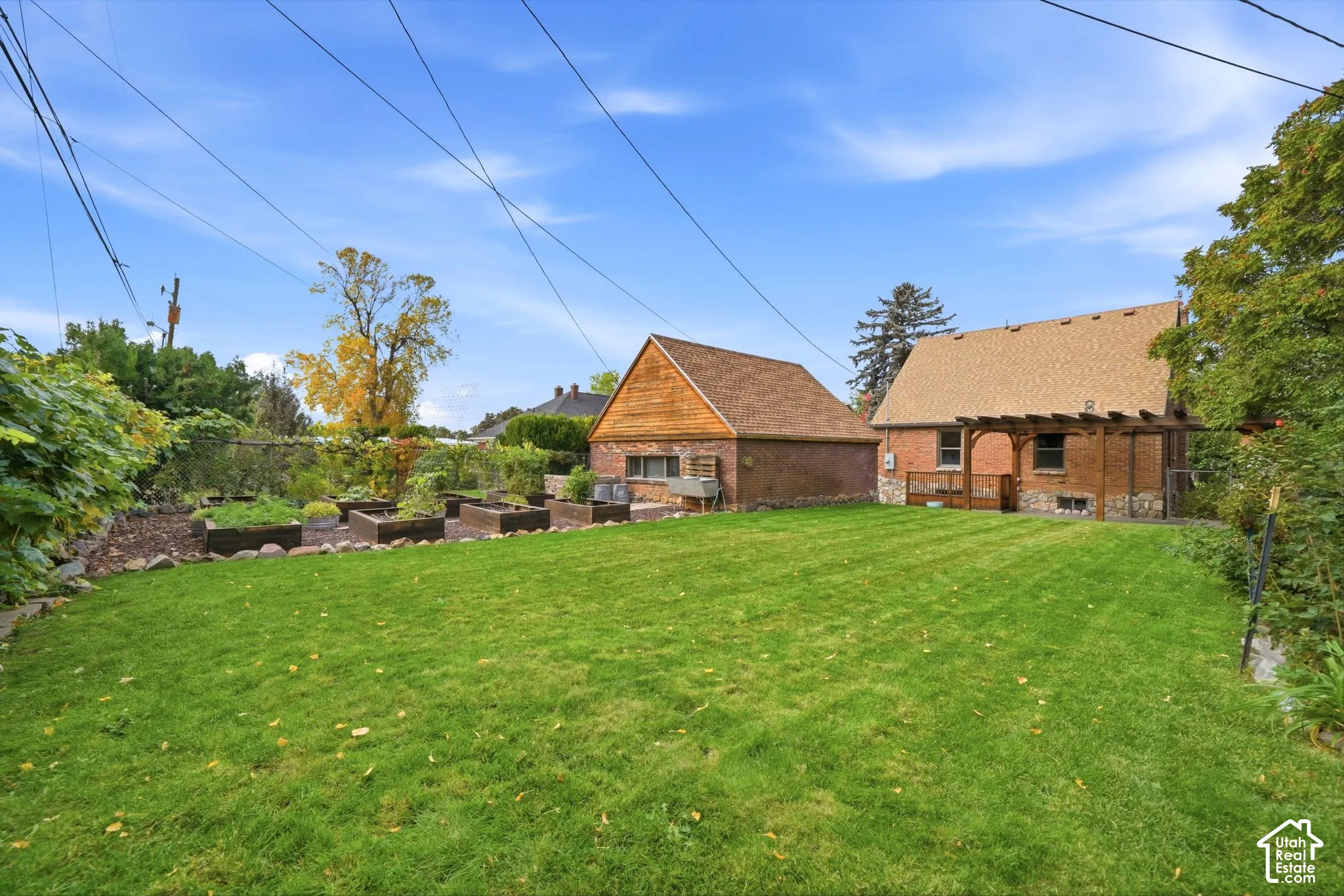 Expansive backyard featuring a grass lawn, raised garden beds, a detached brick garage, and a wooden pergola