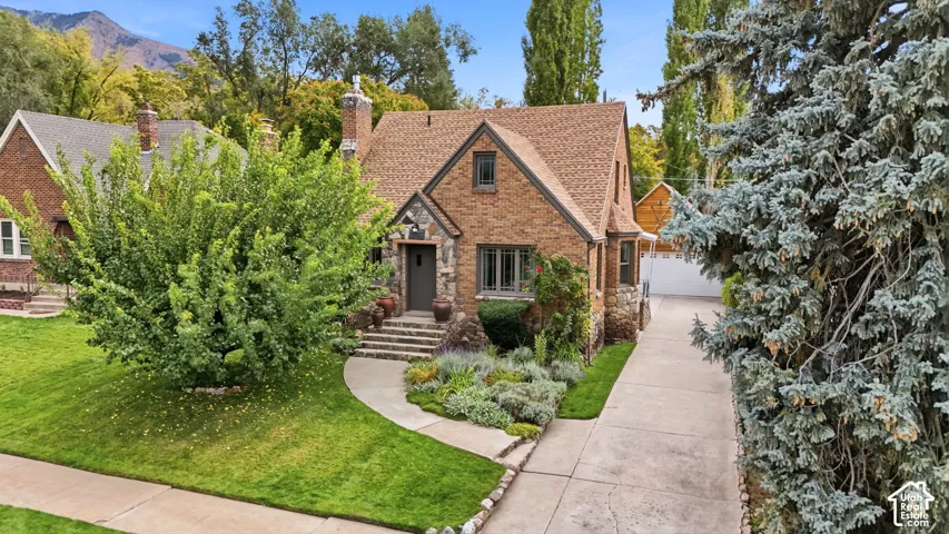 Brick exterior featuring stone accents, a steep-pitched roofline, a concrete driveway, and mountain scenery