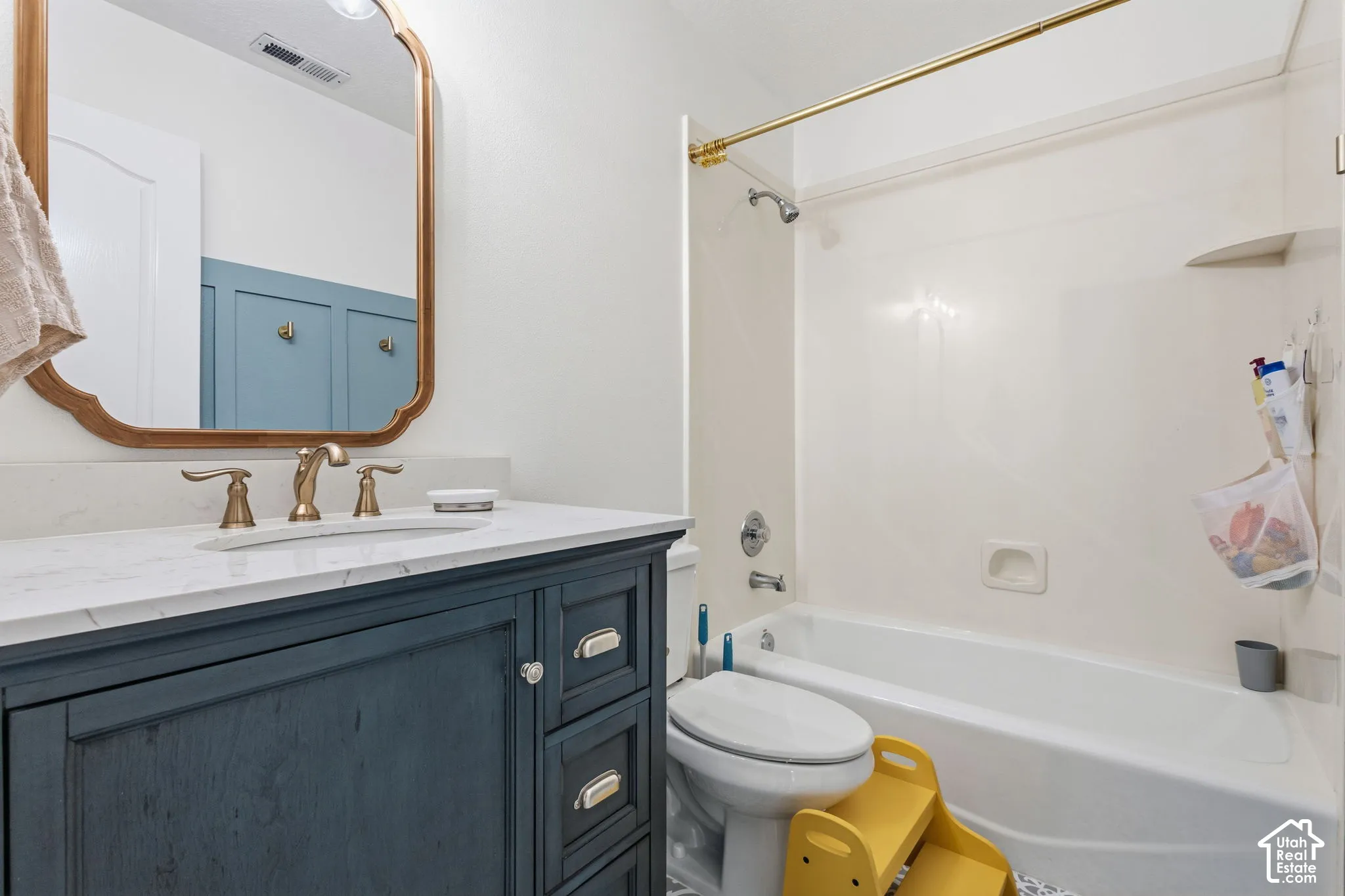 Bathroom vanity featuring a stone-surface countertop, gold-tone faucet, arched mirror, and navy blue cabinetry, complemented by a white tub-and-shower enclosure with gold-tone hardware