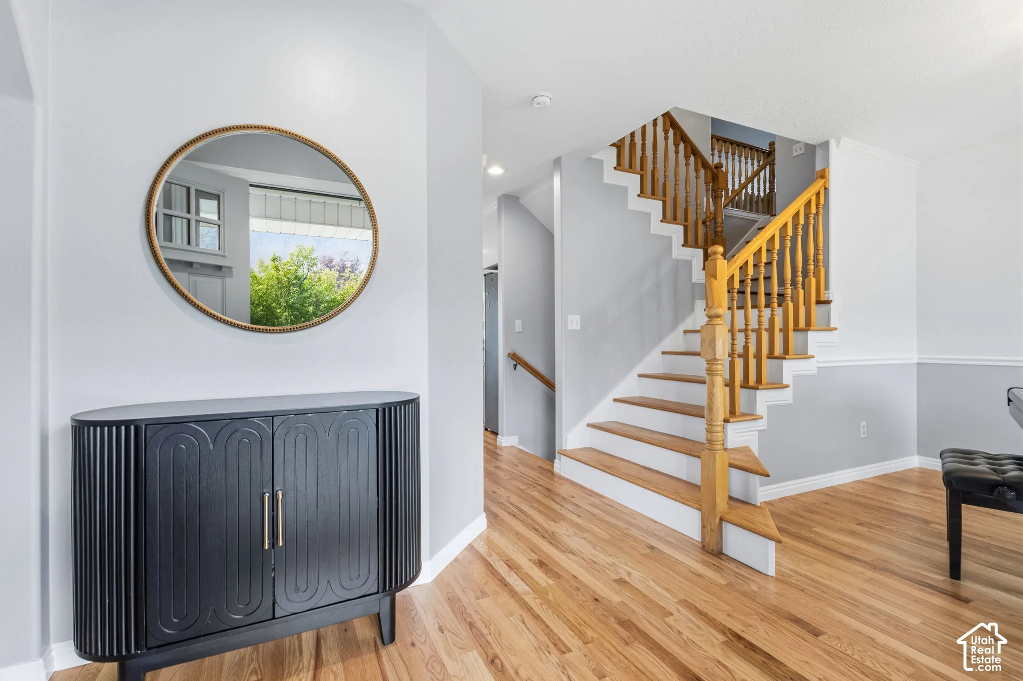Foyer featuring wood-finish flooring, a staircase with a wooden balustrade, and a round wall-mounted mirror